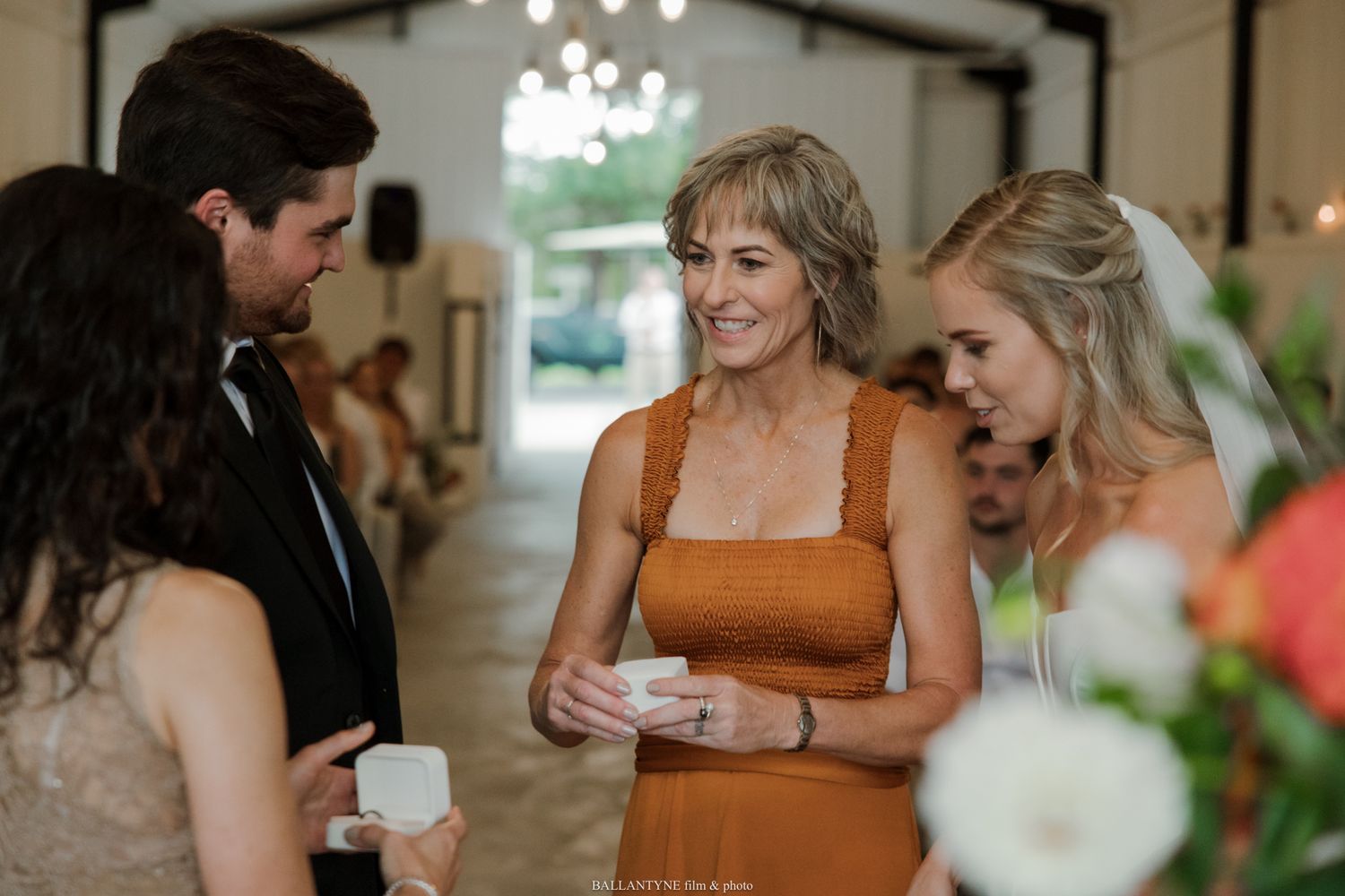 Guests in formal attire chat and laugh together inside an elegant wedding venue with chandelier lighting.