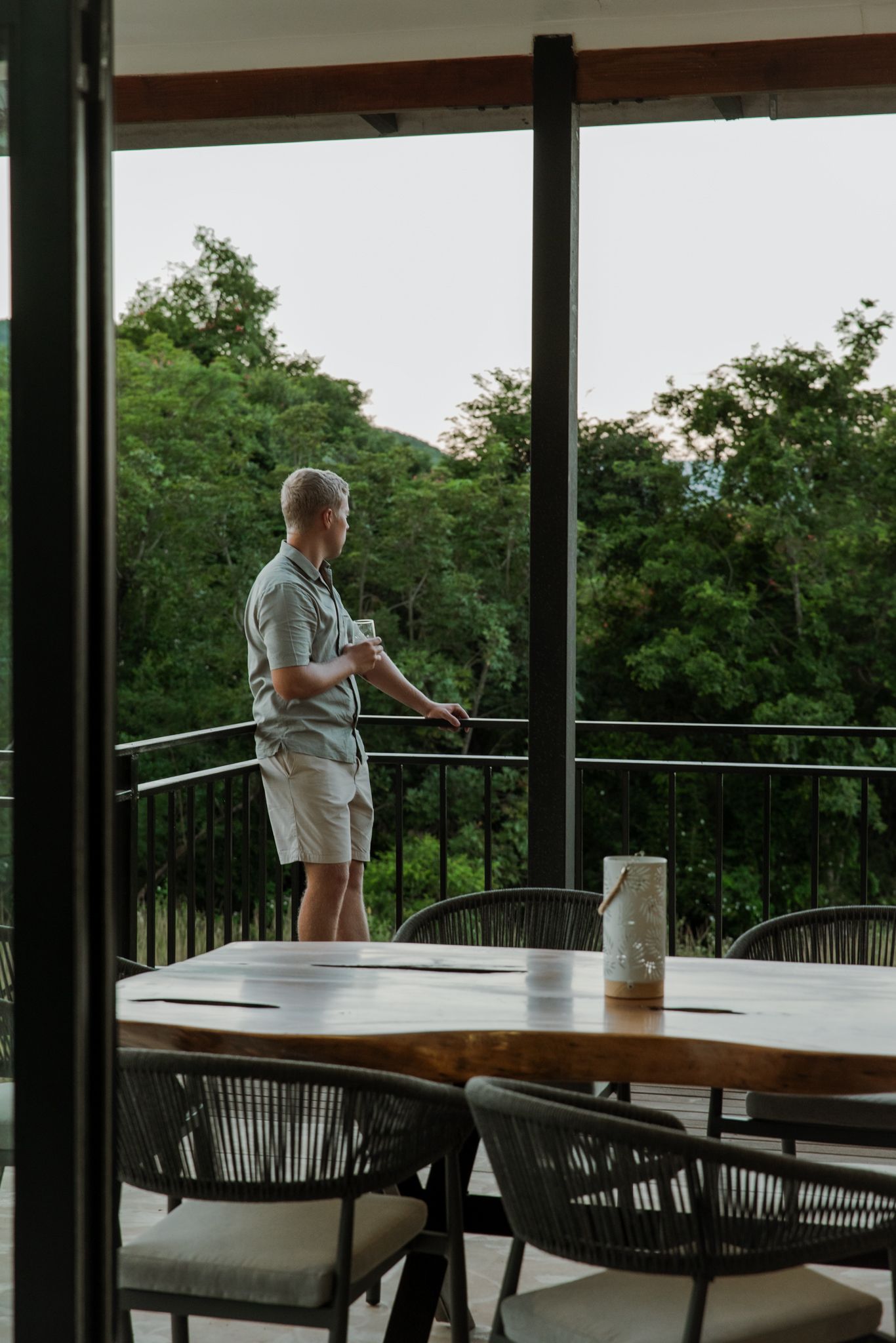 A covered outdoor dining area with tables and chairs overlooking a lush green forest view through large windows.