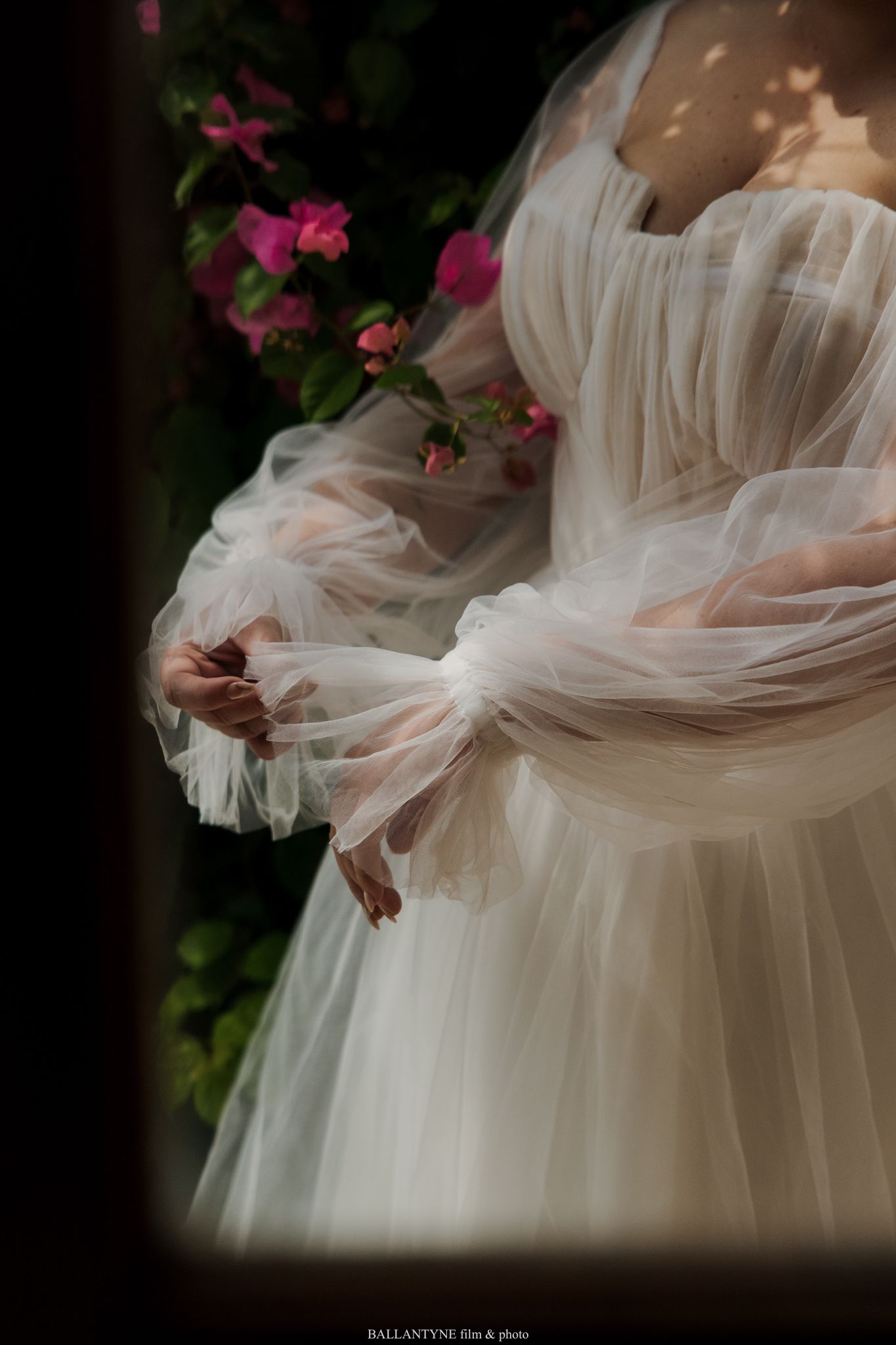Delicate white tulle fabric of a wedding dress with pink flowers in the background.