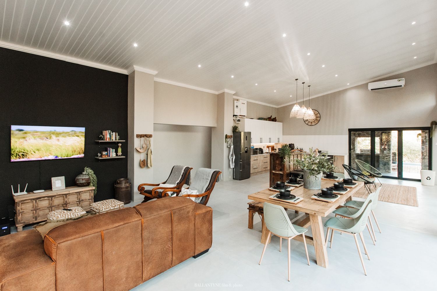Modern open concept living room with brown leather sofa, dining area and black accent wall featuring mounted TV.