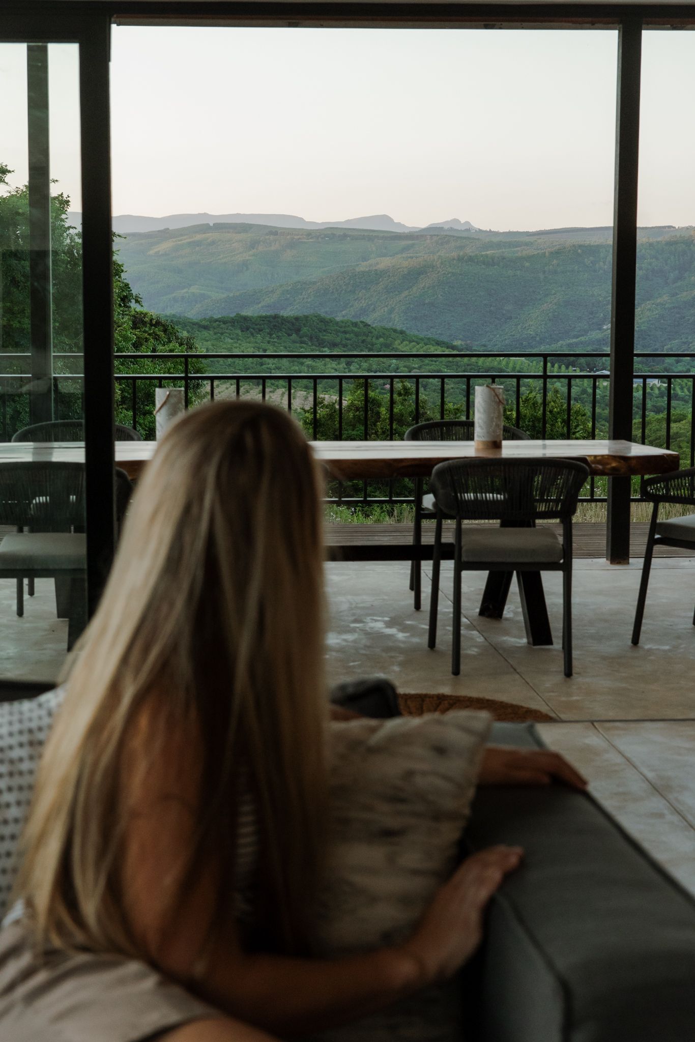 A serene mountain view from a covered patio with tables and chairs overlooking a lush green landscape.