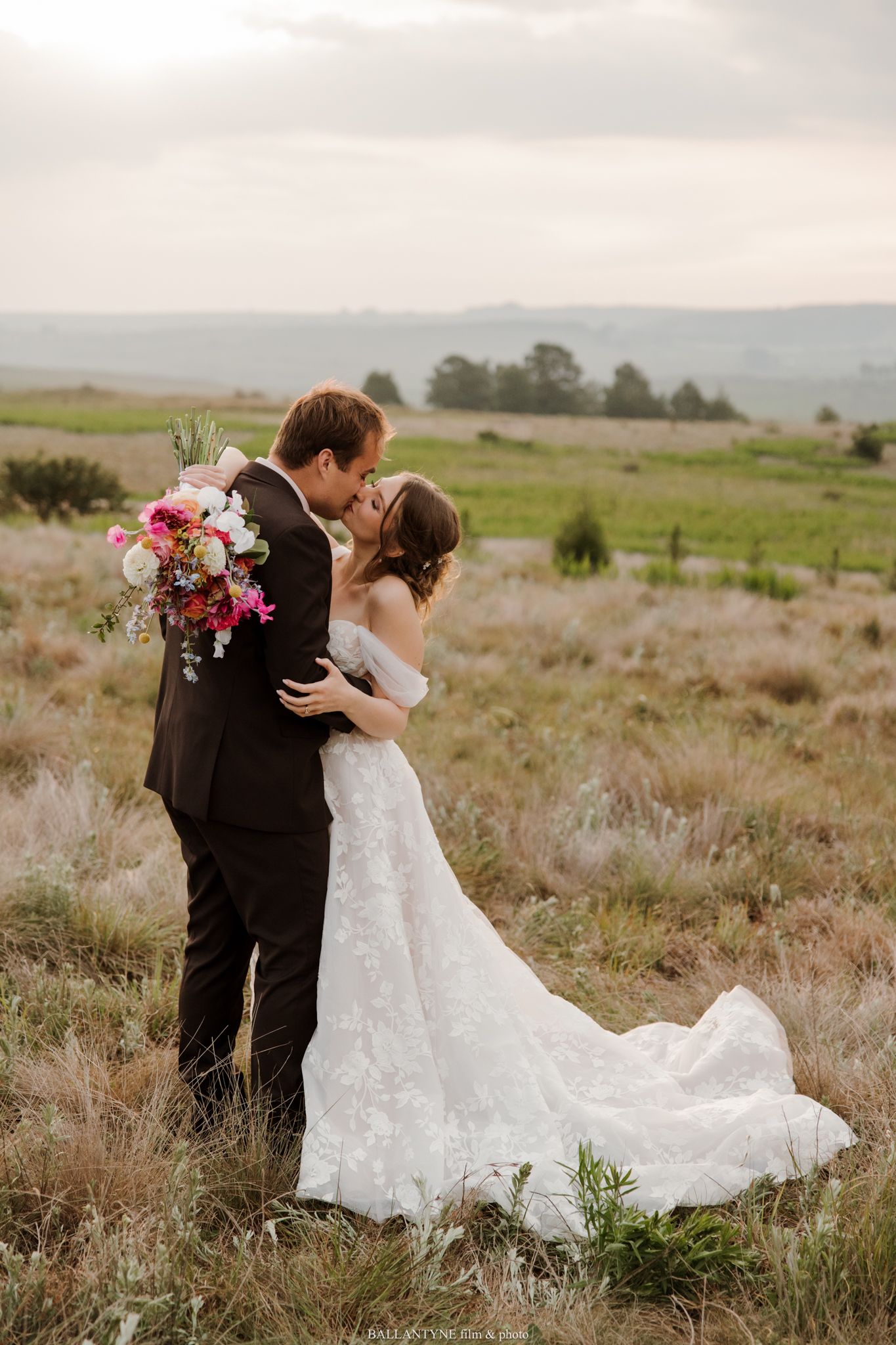 A romantic wedding couple embracing in a scenic field during golden hour.