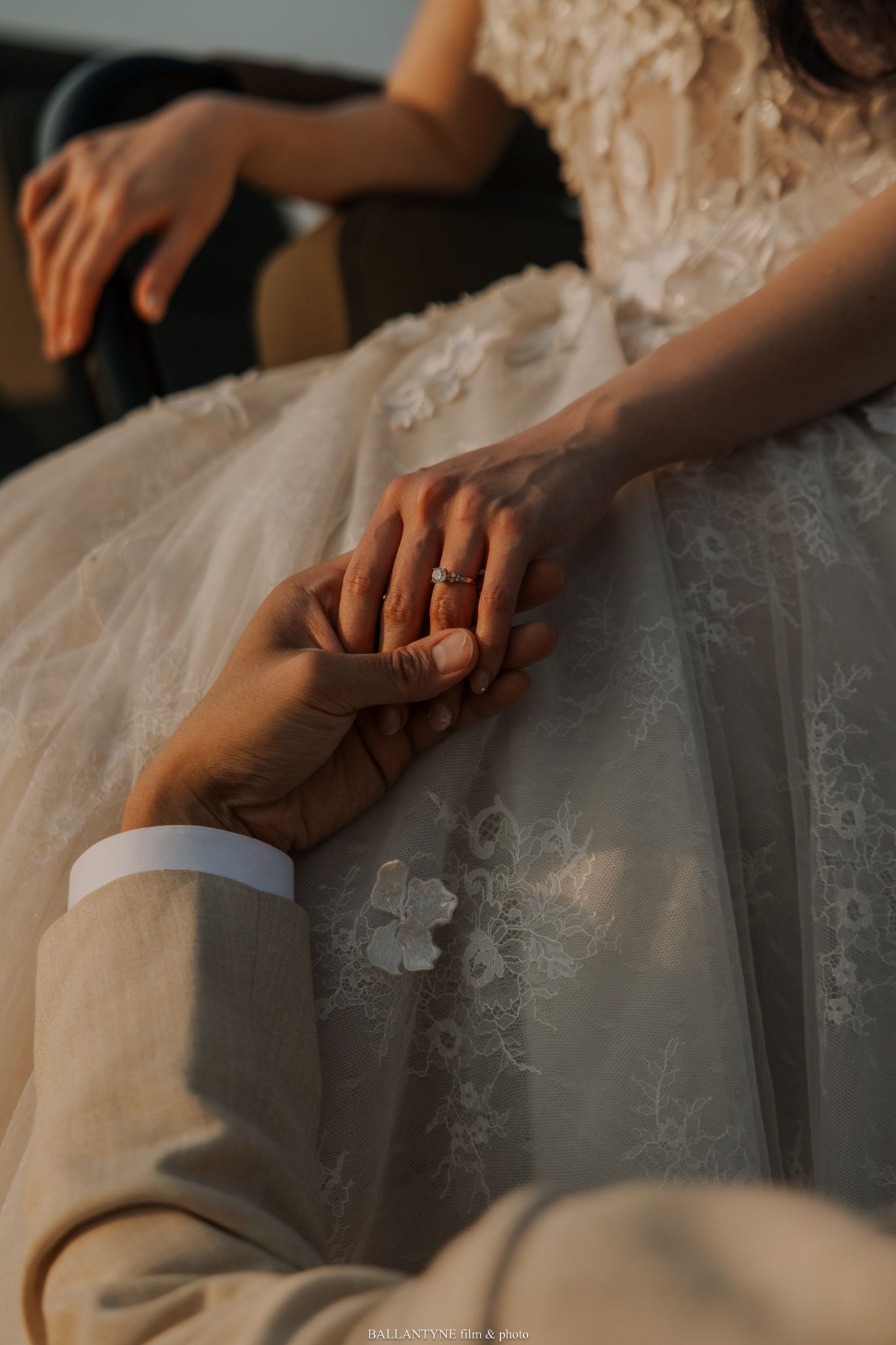 Close-up details of hands touching intricate lace and beadwork on a wedding gown.