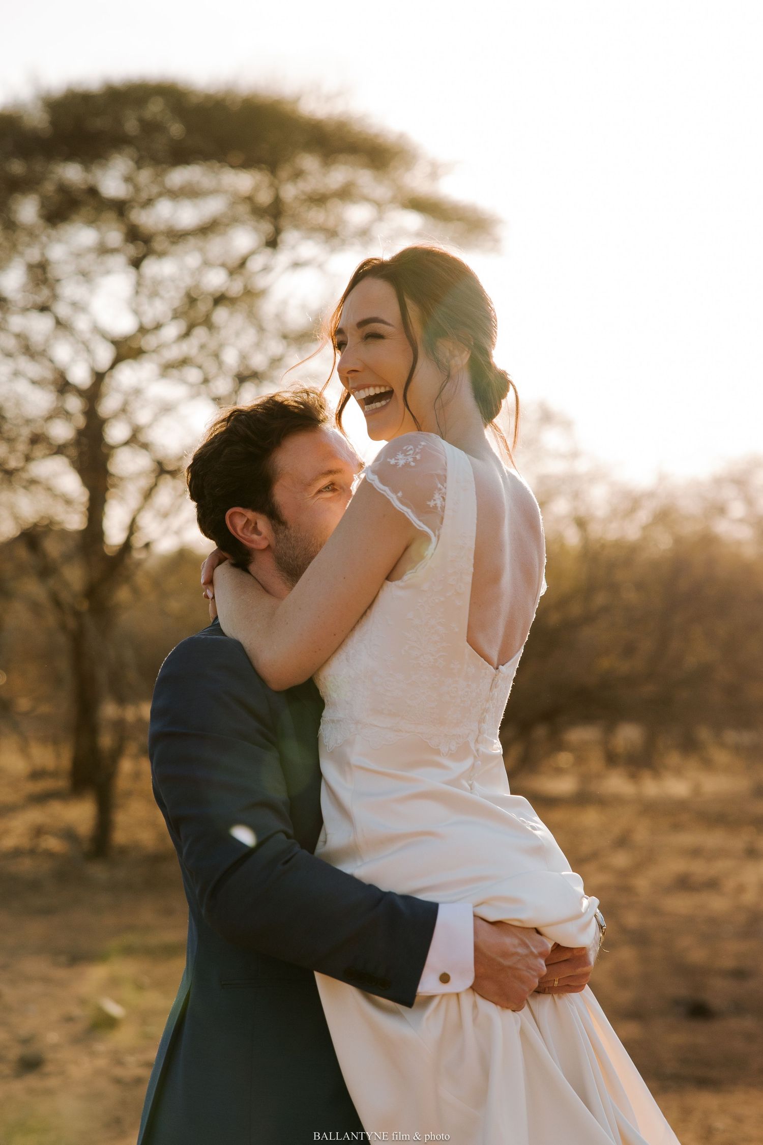 A sunset wedding photo captures a couple sharing a joyful embrace in golden light.