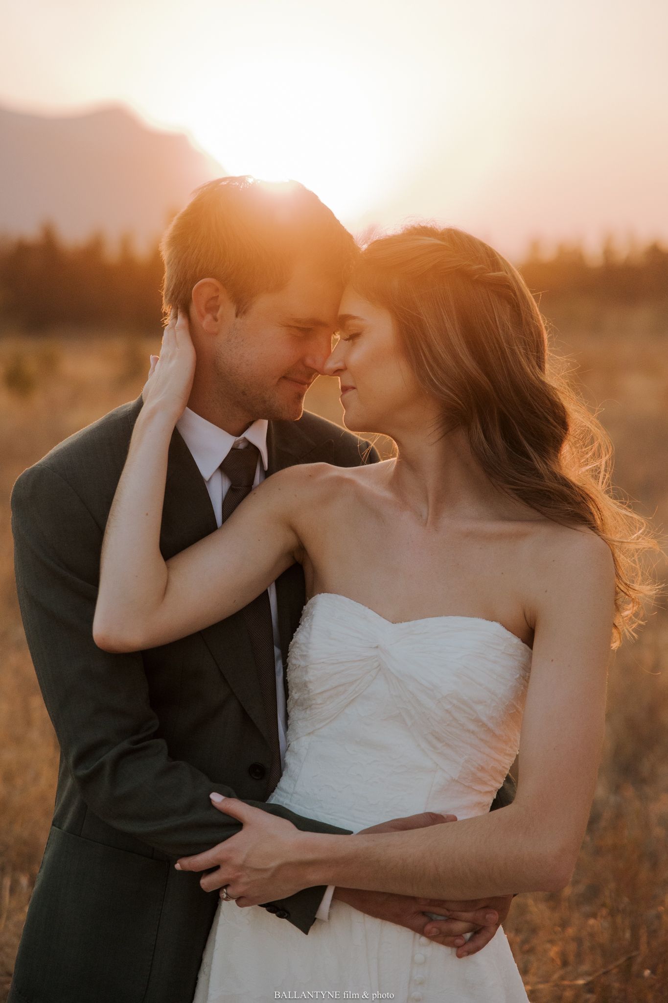Romantic sunset portrait of a couple in wedding attire in a golden field.