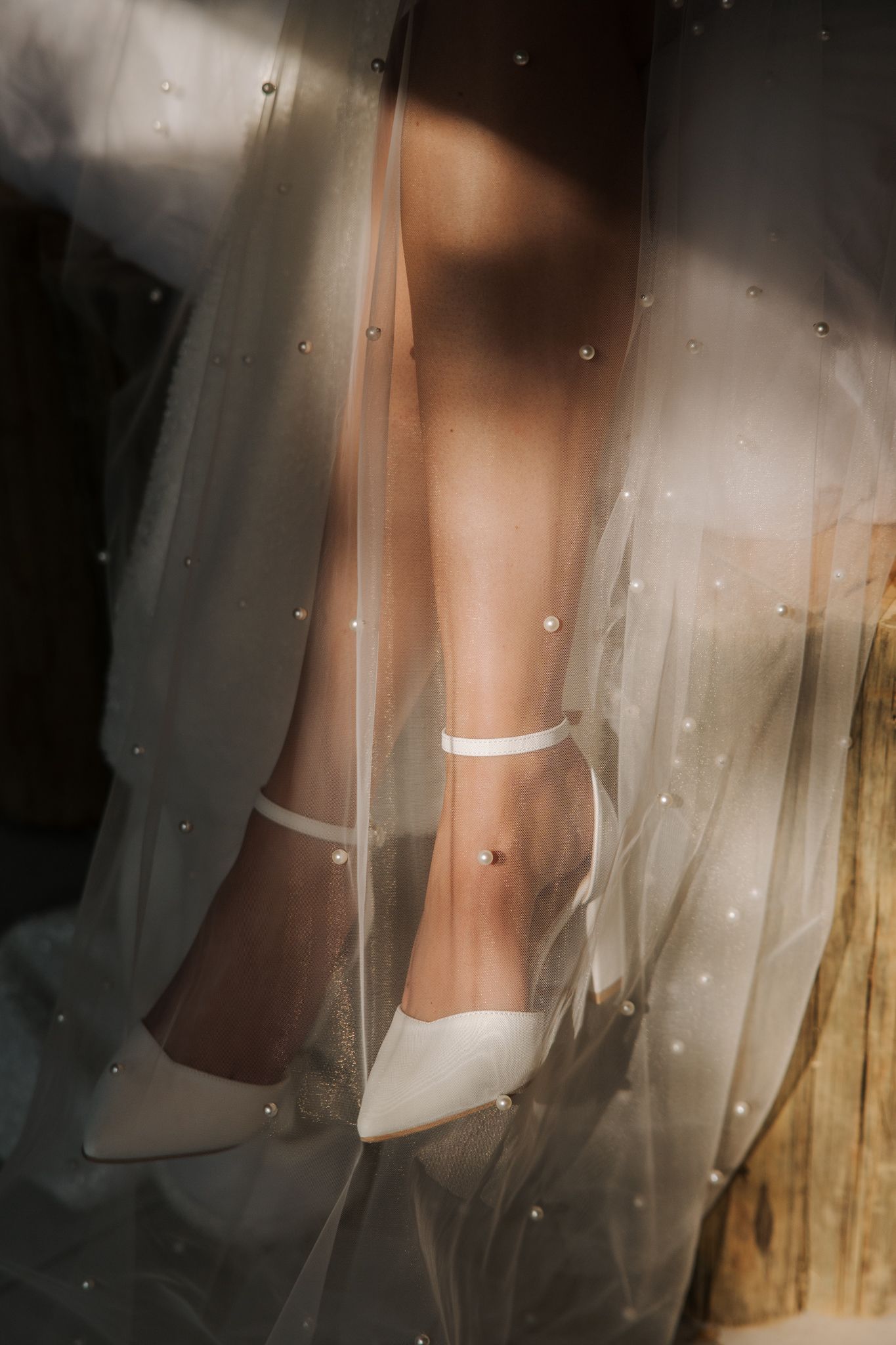White wedding shoes peek through delicate tulle veil in a dreamy, soft-focus photograph.