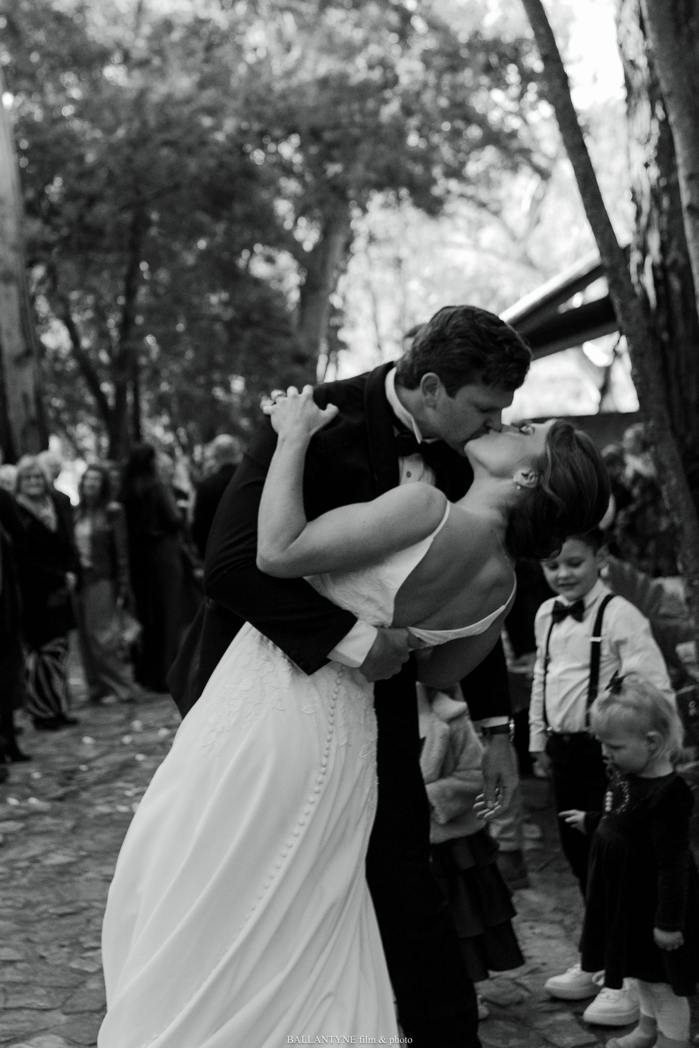 Black and white wedding photo capturing a romantic dip kiss during an outdoor ceremony.