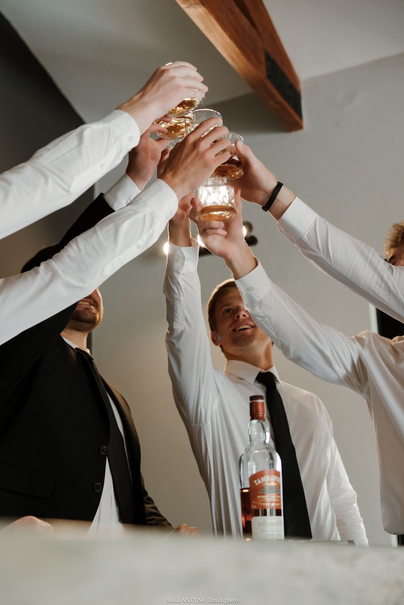 Group of men in dress shirts raising glasses of whiskey in a celebratory toast indoors.