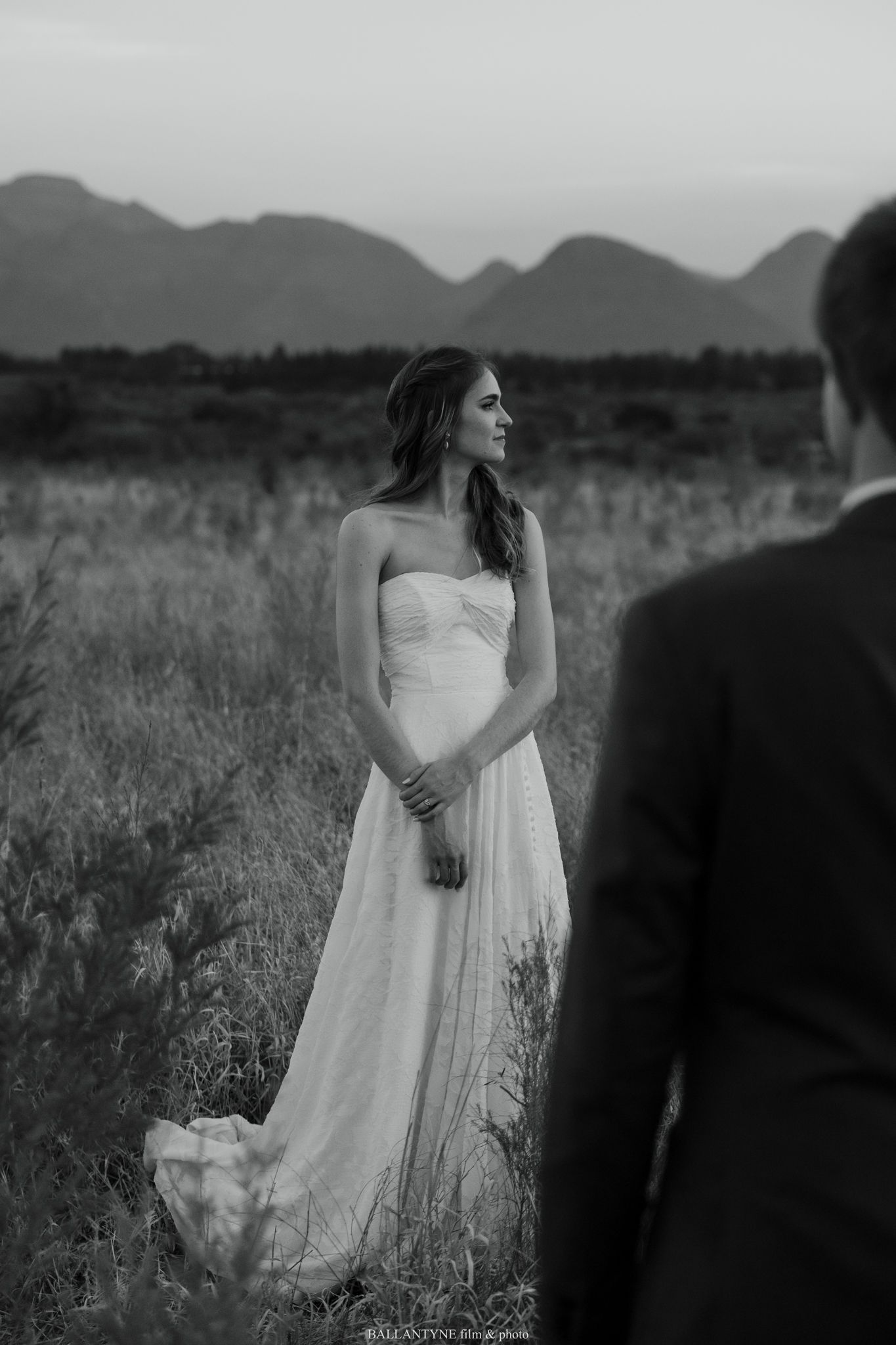 Black and white portrait of bride in flowing dress against mountain landscape.