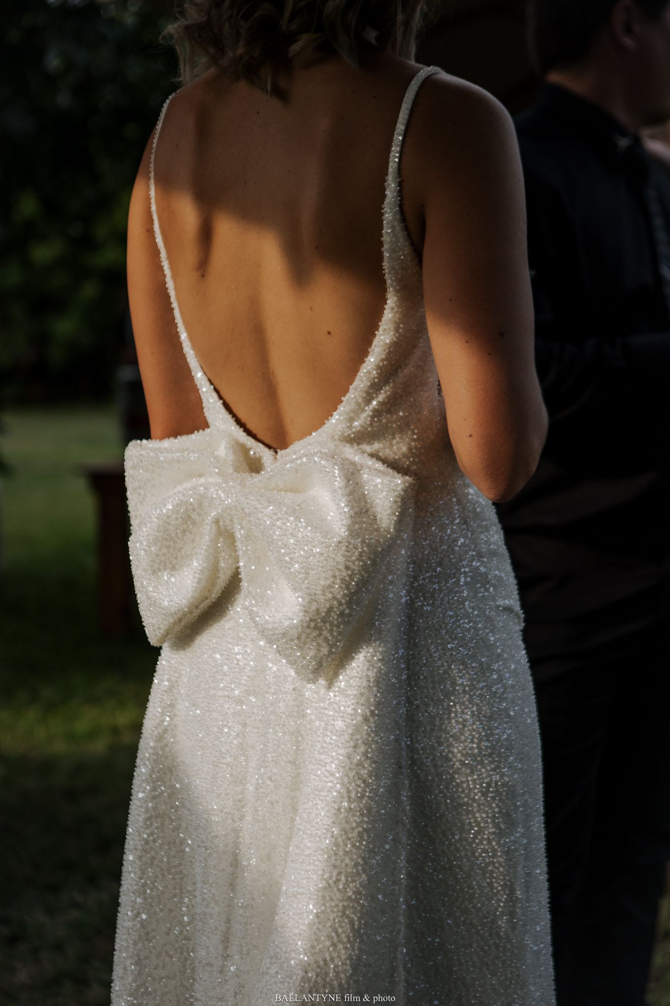 Close-up detail of a sparkly white wedding dress with thin straps against a dark background.