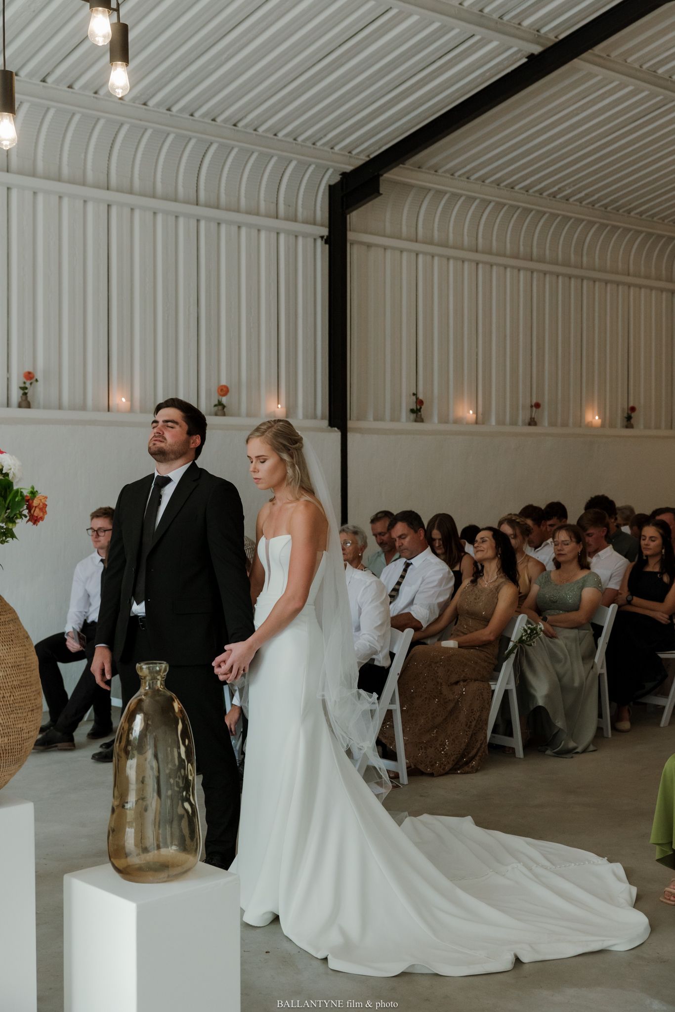 Bride and groom stand at the altar during an elegant indoor wedding ceremony with seated guests in the background.