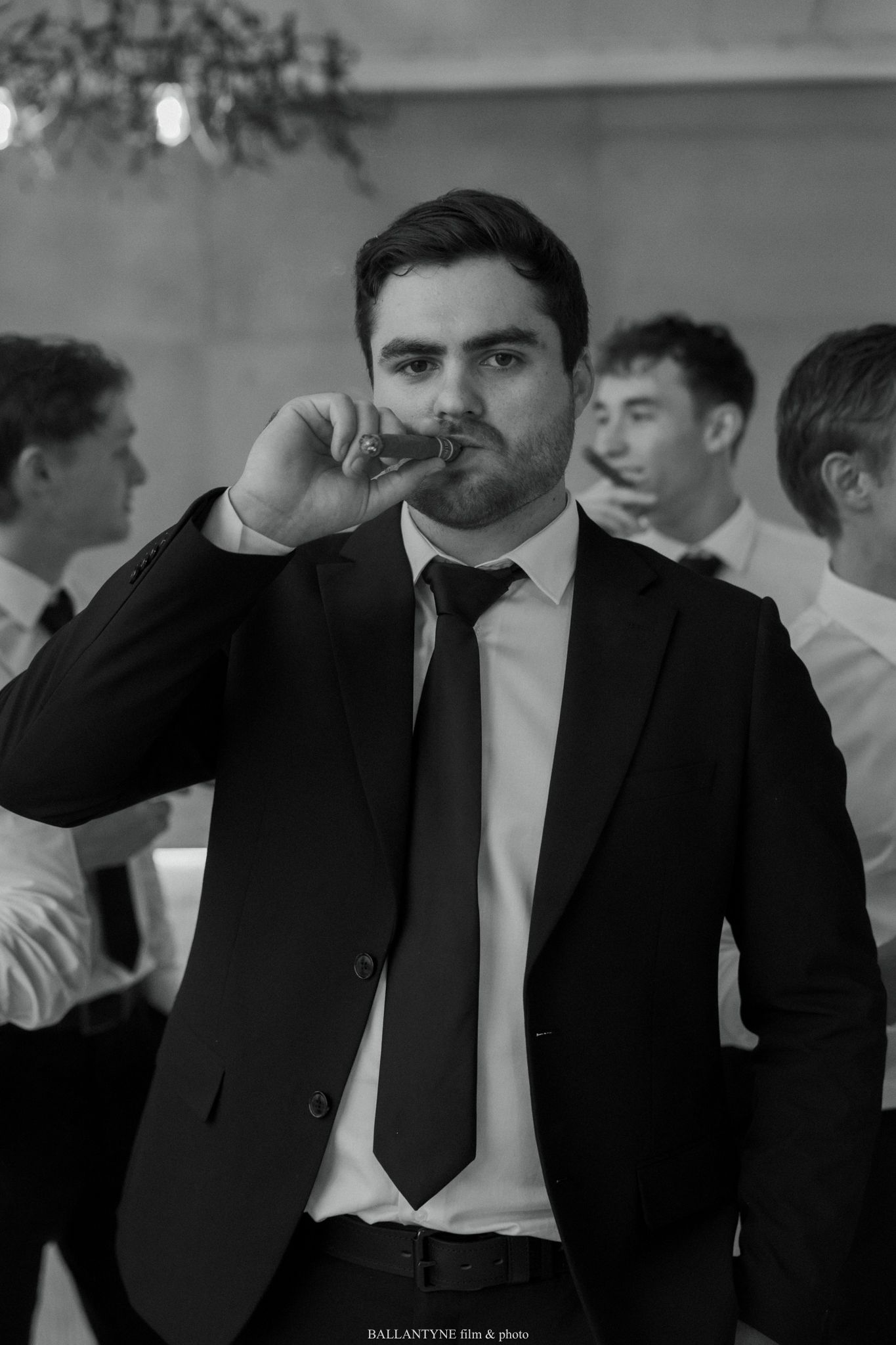 Black and white photo of a man in a suit smoking a cigar at a formal event.