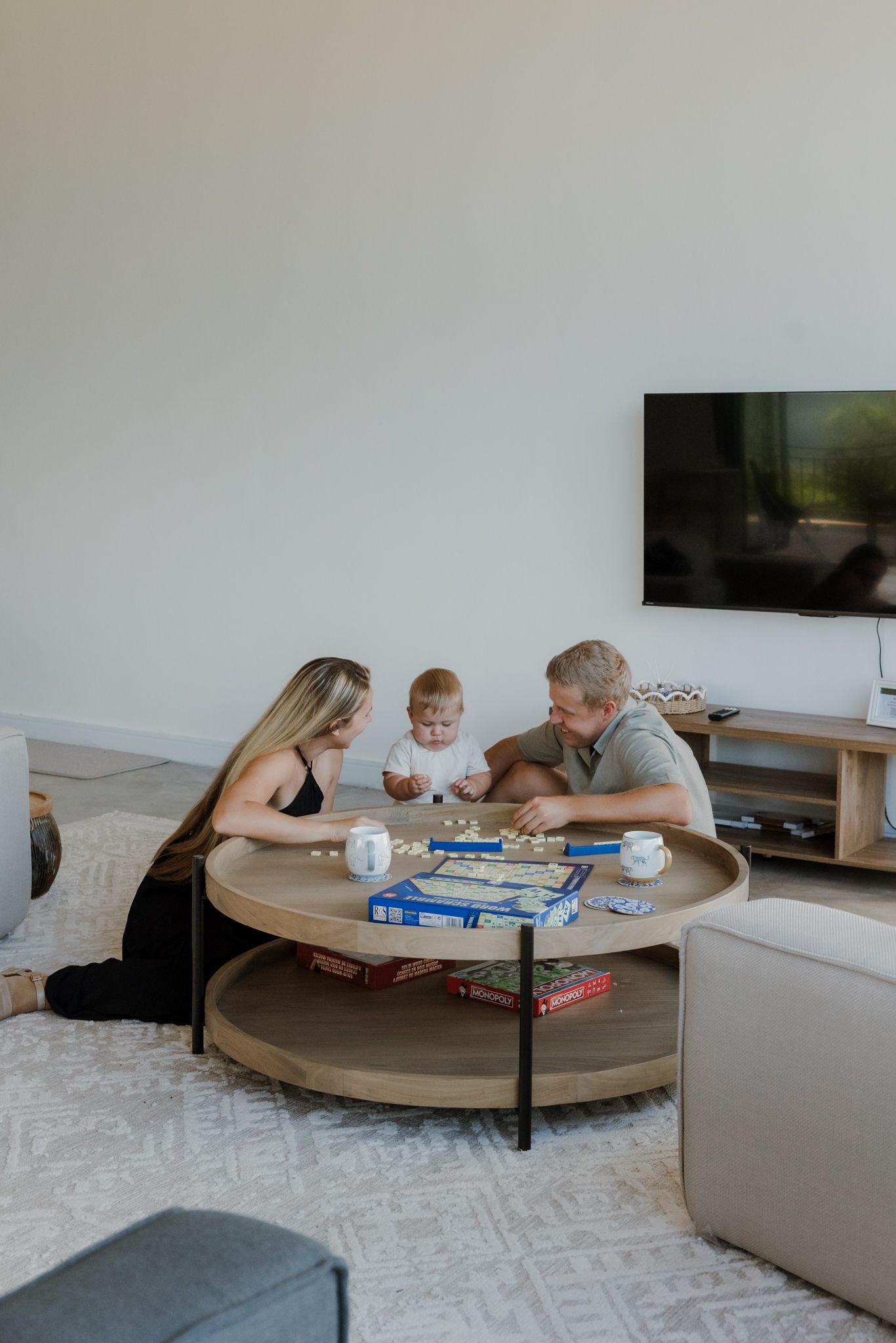 People gathered around a round wooden coffee table playing board games in a modern living room.