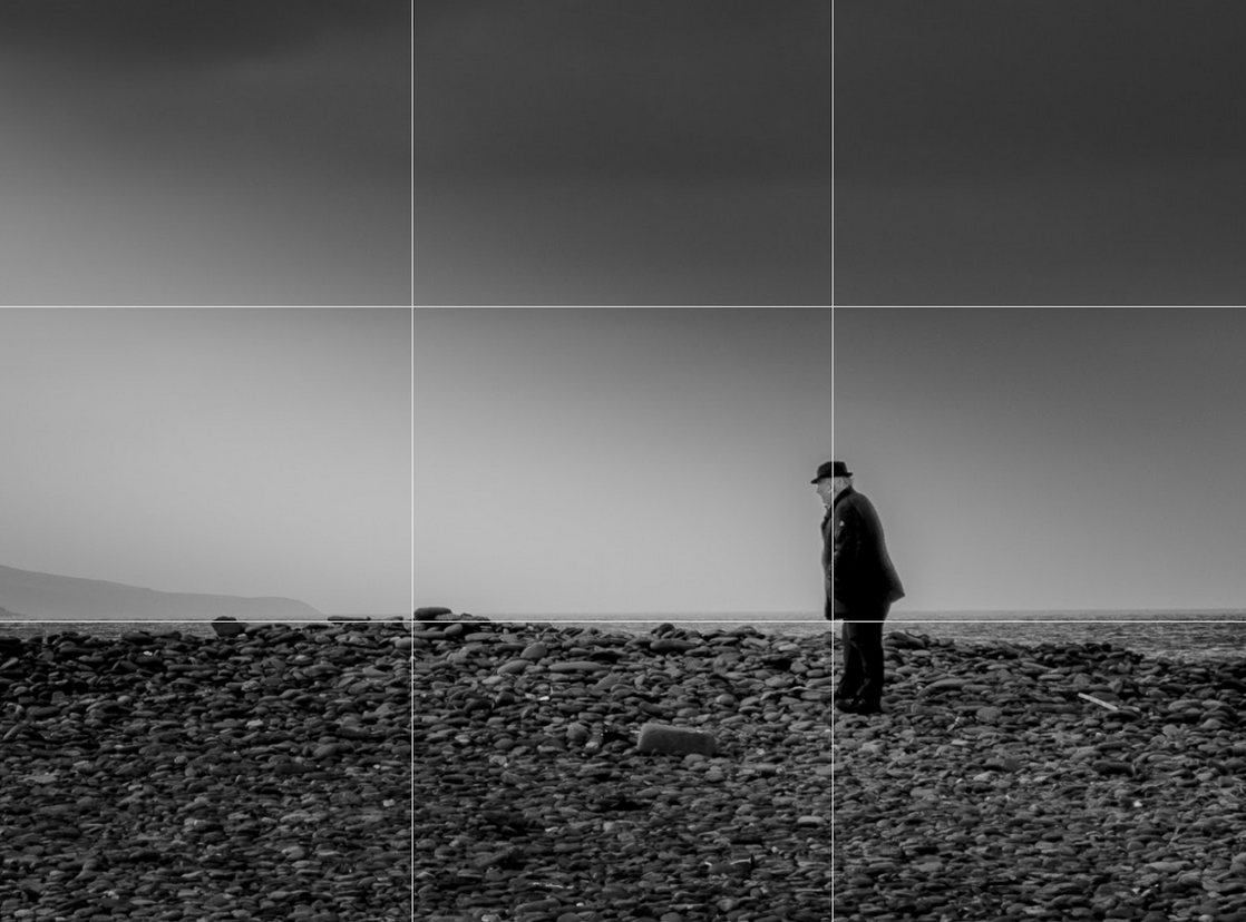 old man in suit standing landscape on stony beach black and white