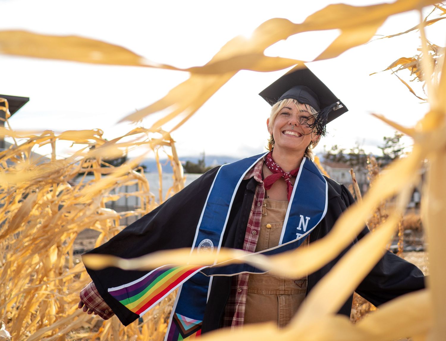 landscape graduate smiling in cornfield sun behind, wearing overalls