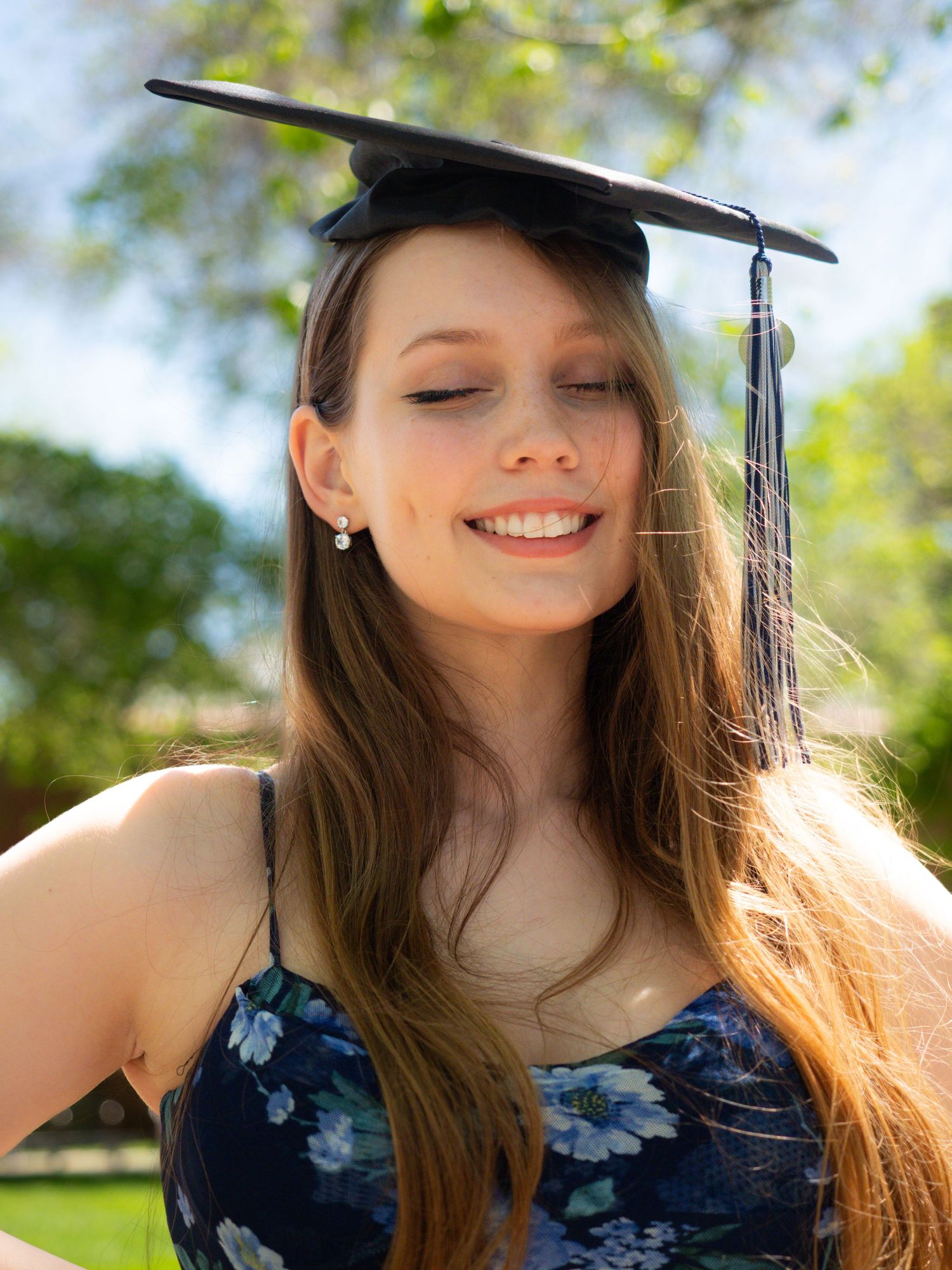 portrait smiling graduate photo woman blue outfit, cap and tassel spring background