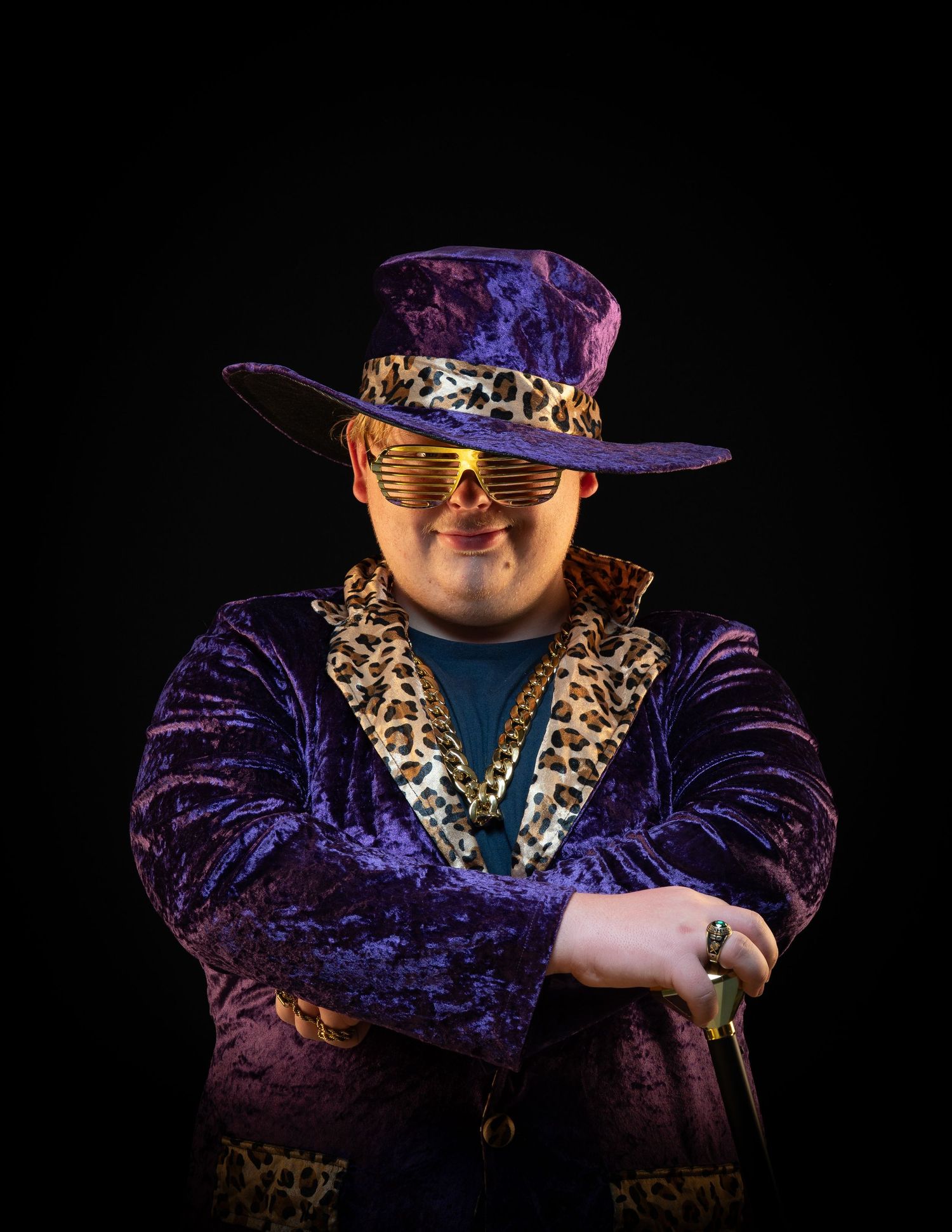man purple halloween costume holding cane crossed arms portrait black background