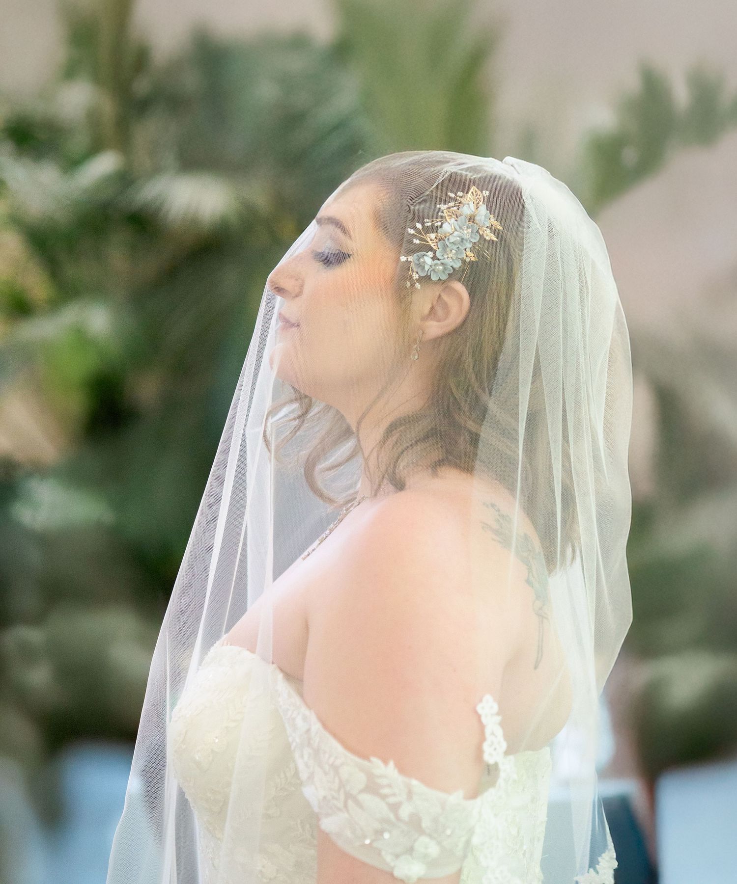 woman side view wedding portrait veil covering face green background white dress short hair