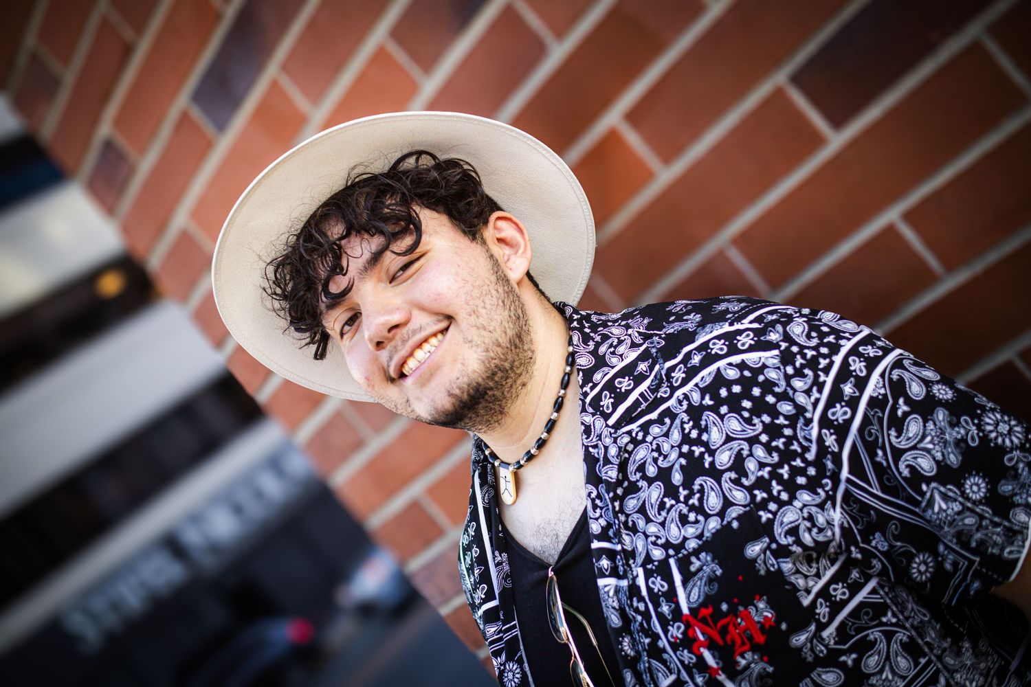 man wide brim hat curly hair smiling back to brick wall landscape