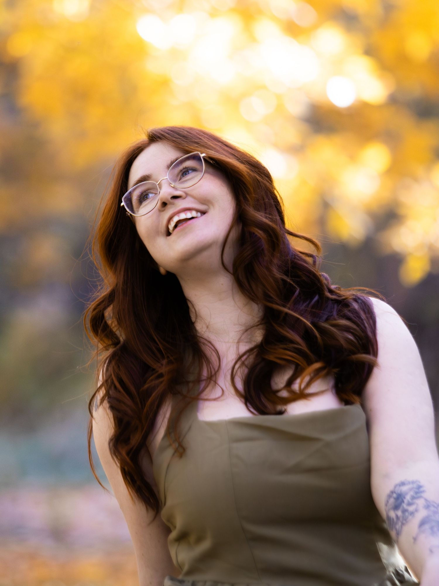 woman smiling portrait graduation photo looking up blurry background wavy red hair green dress