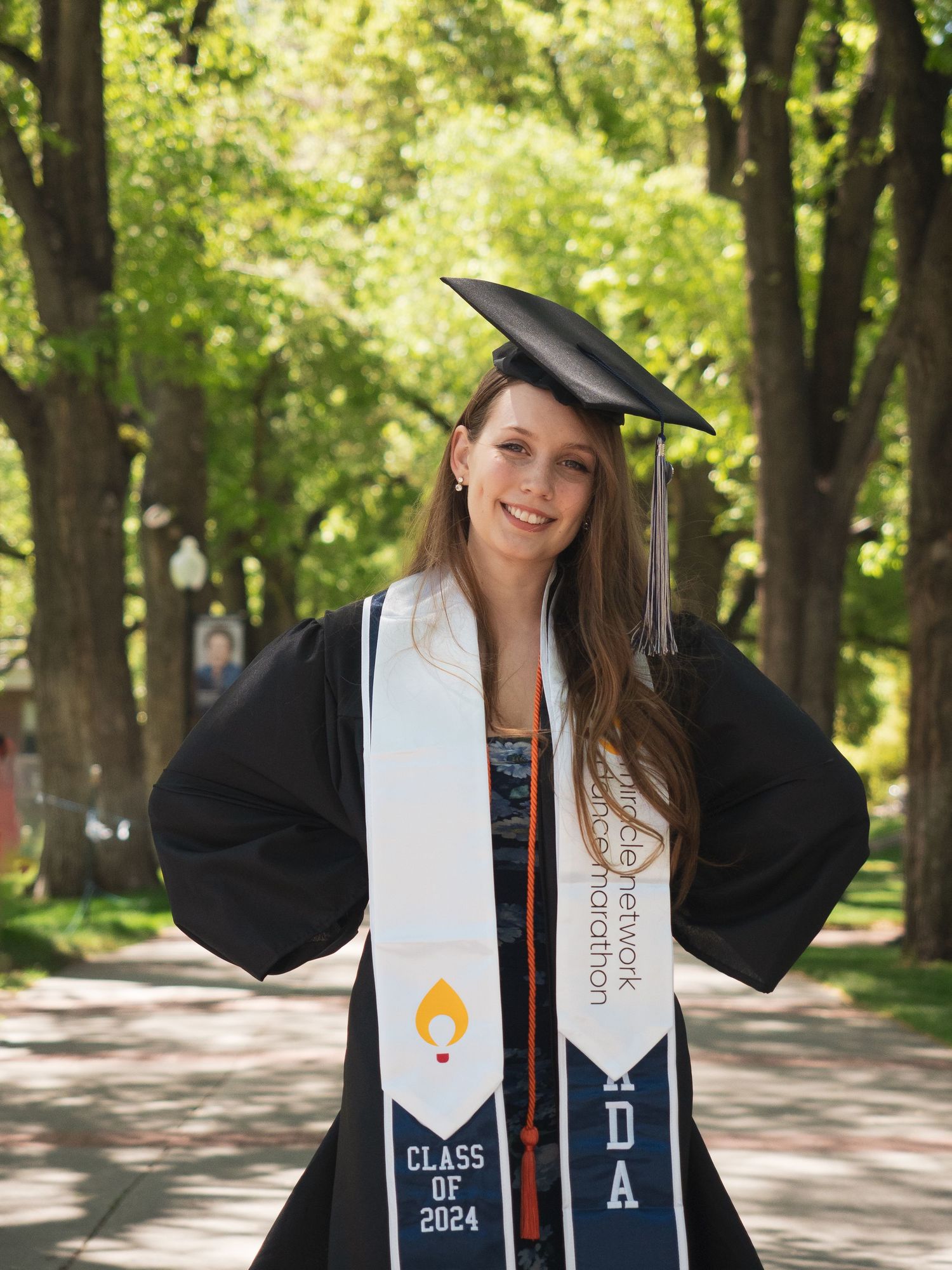 woman grad portrait cap and gown UNR green background smile hands on hips