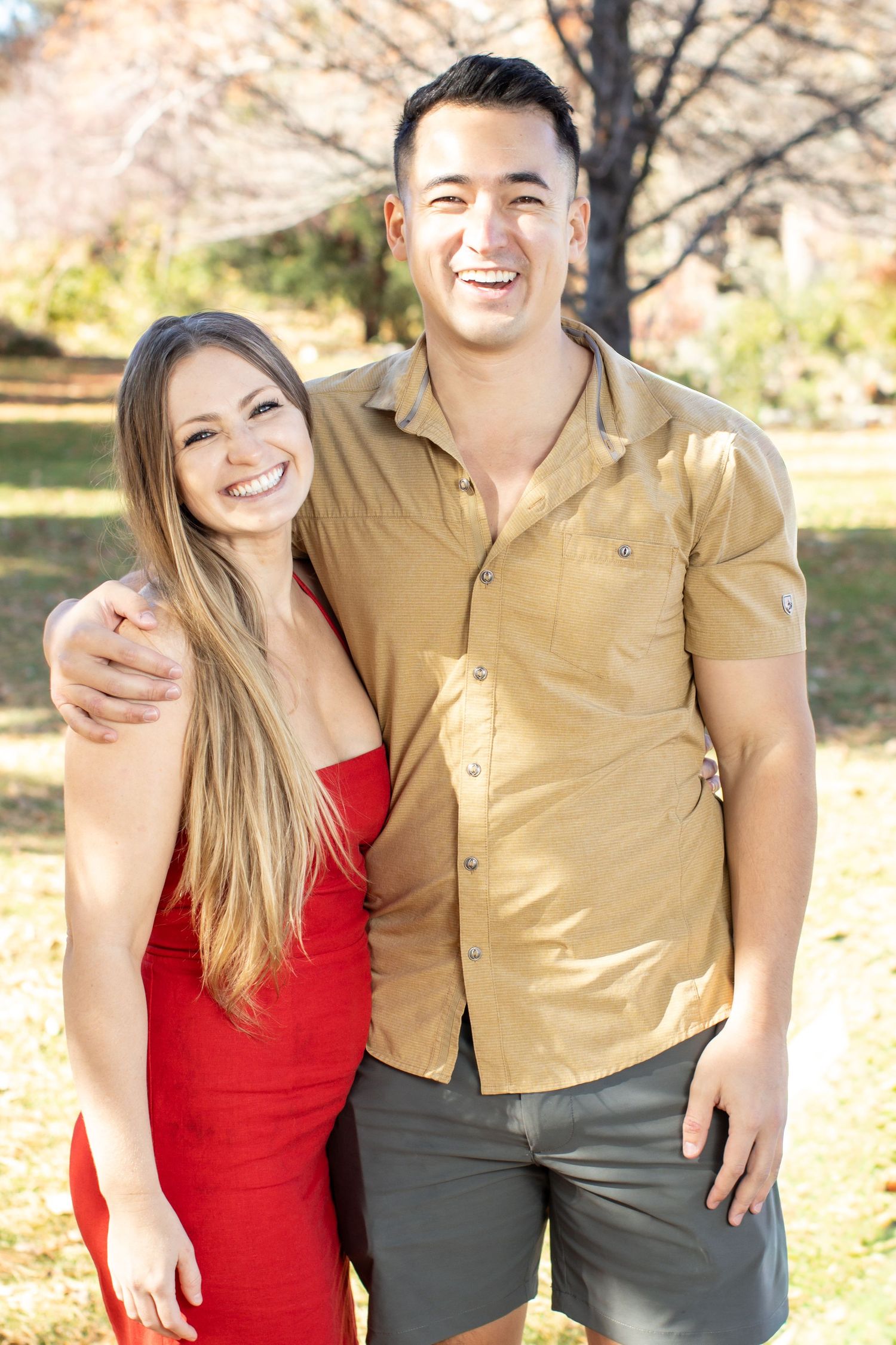 couple, nature background, red dress and tan shirt smiling hand over shoulder