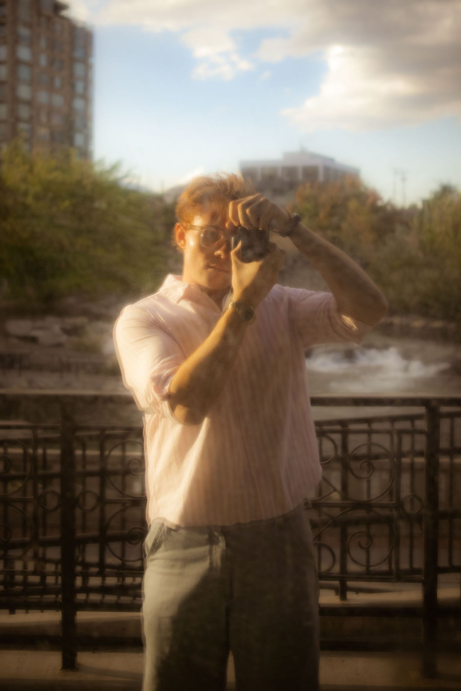 photographer holding camera photographing self in mirror, pink shirt city background