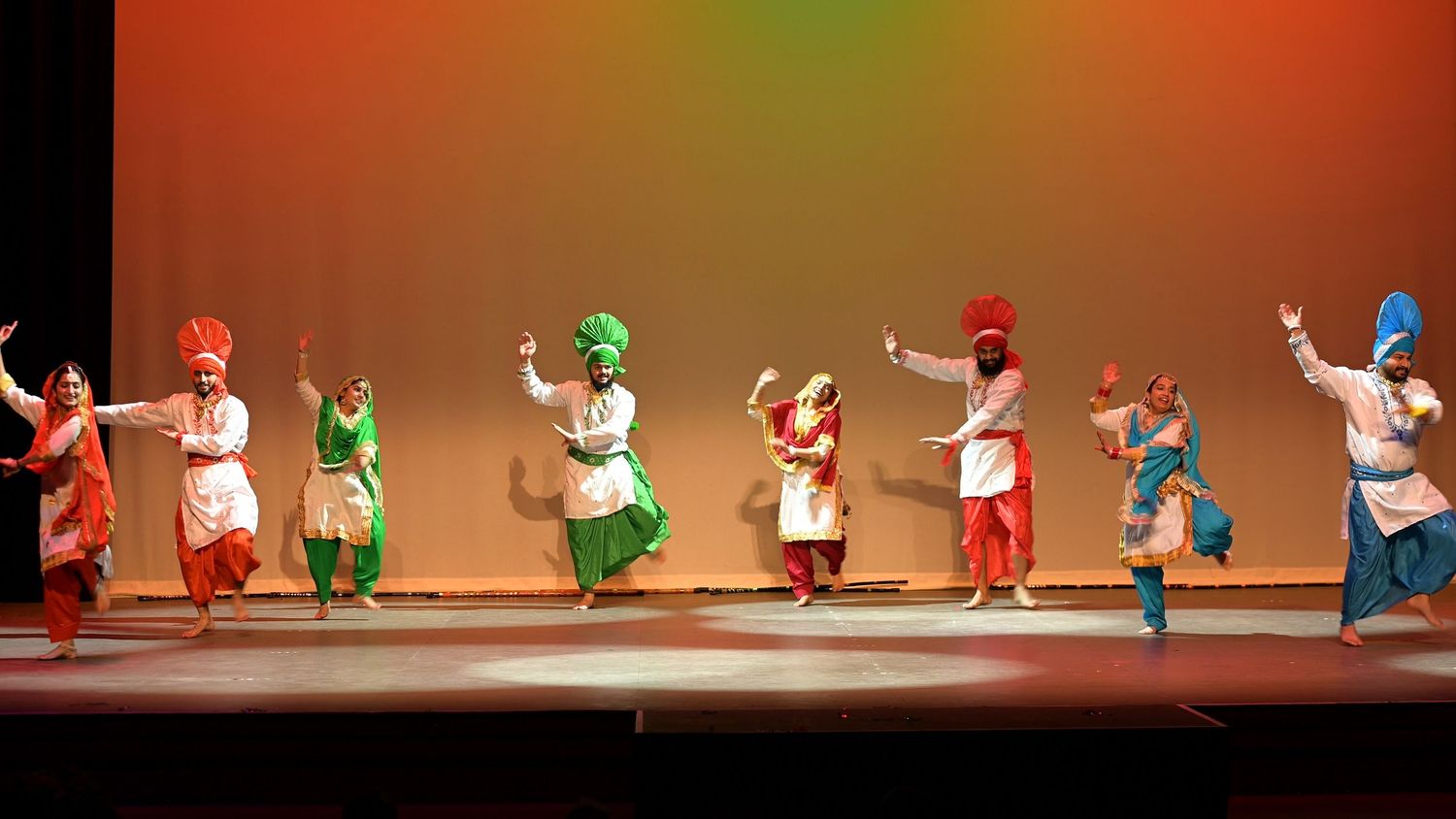 Colourful traditional Indian dance performance on stage with dancers in vibrant costumes.