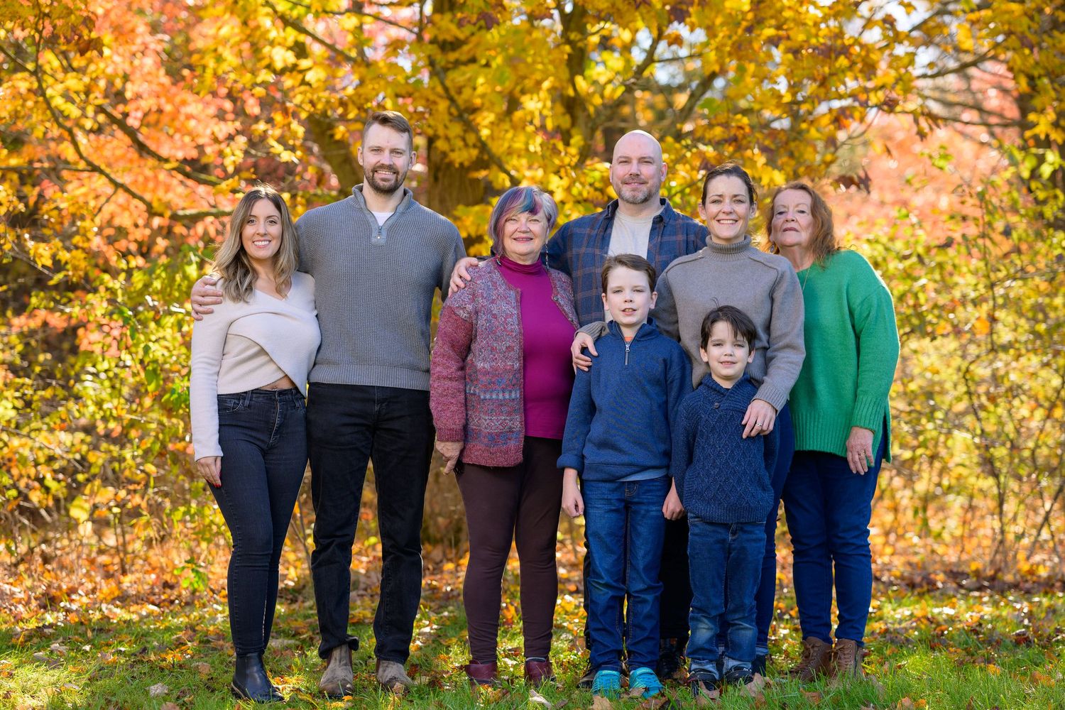 A group stands together outdoors against a backdrop of vibrant autumn foliage with golden yellow and orange leaves.