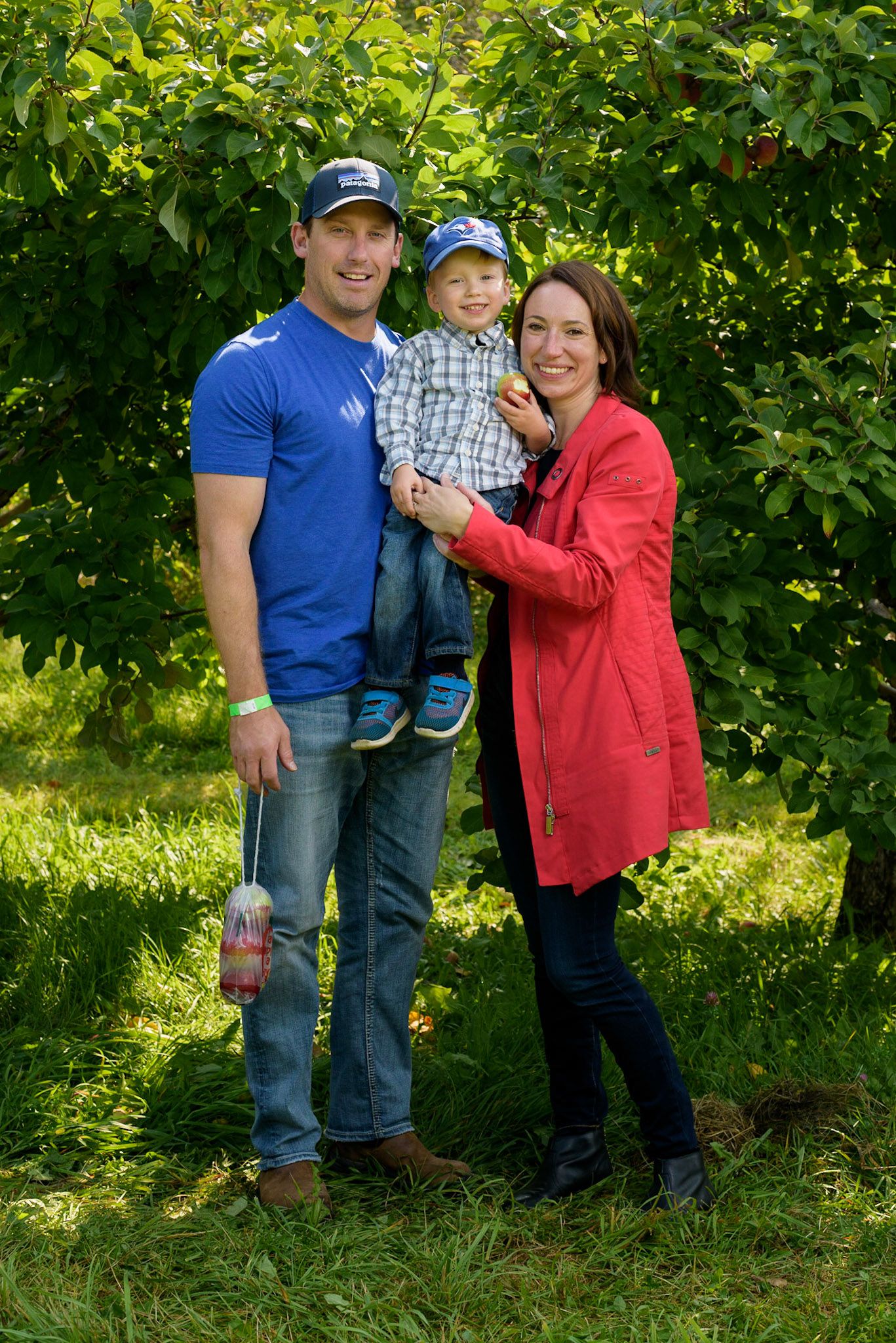 Family portrait outdoors against lush green foliage in casual attire.