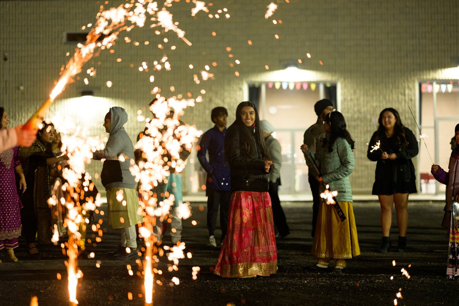 Performers hold sparklers during an outdoor nighttime festival event creating trails of light against the dark sky.
