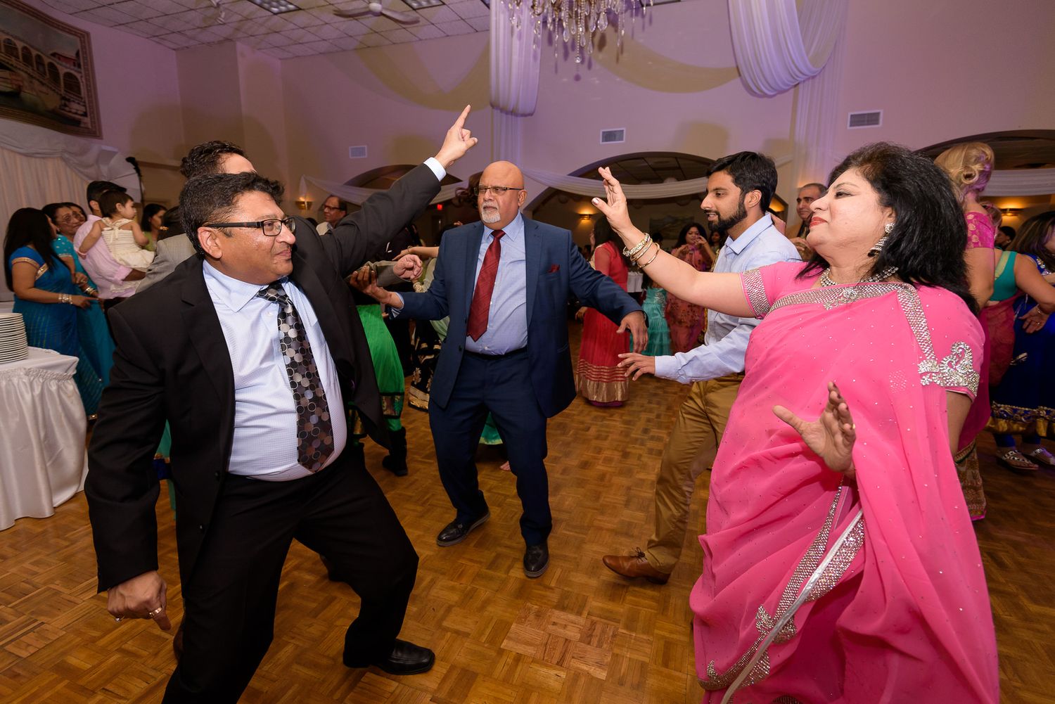 Guests dancing and celebrating at a lively wedding reception with purple lighting.