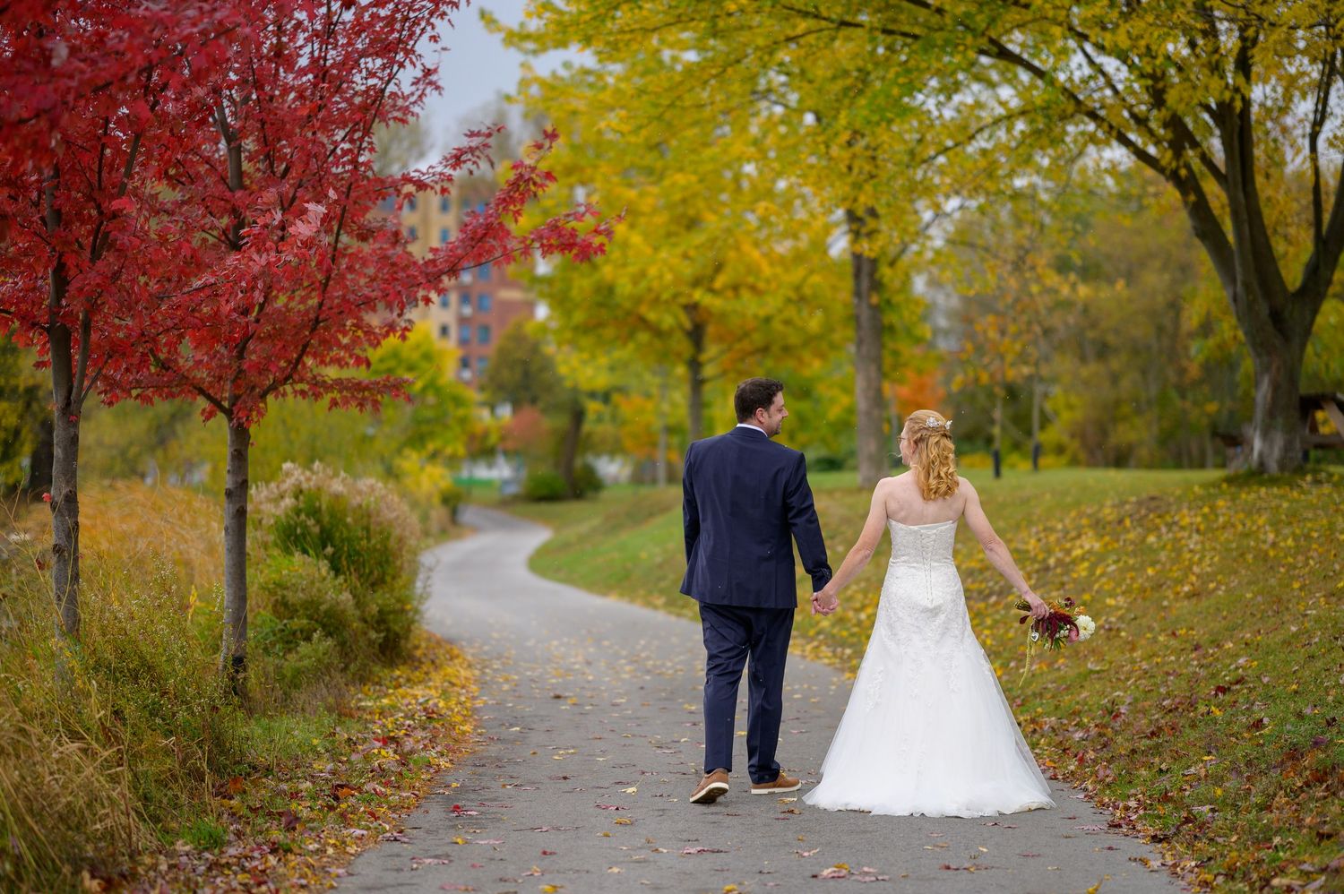 Wedding couple walking along tree-lined path with stunning red and gold autumn colours.