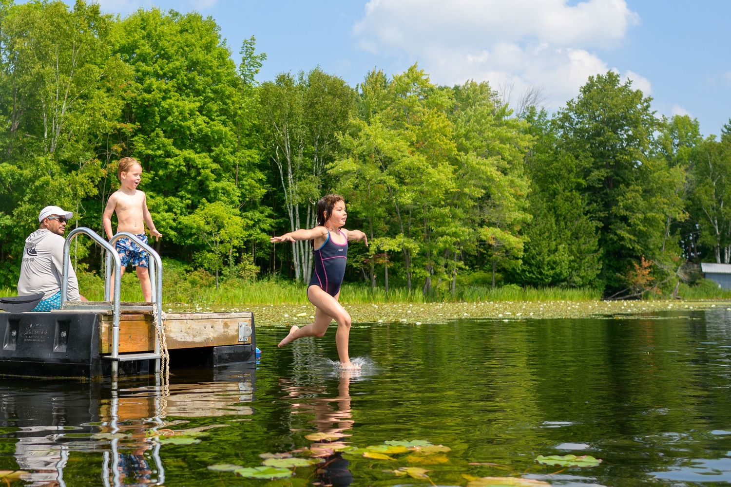 People enjoying a summer day swimming and relaxing at a scenic lake surrounded by lush green trees.