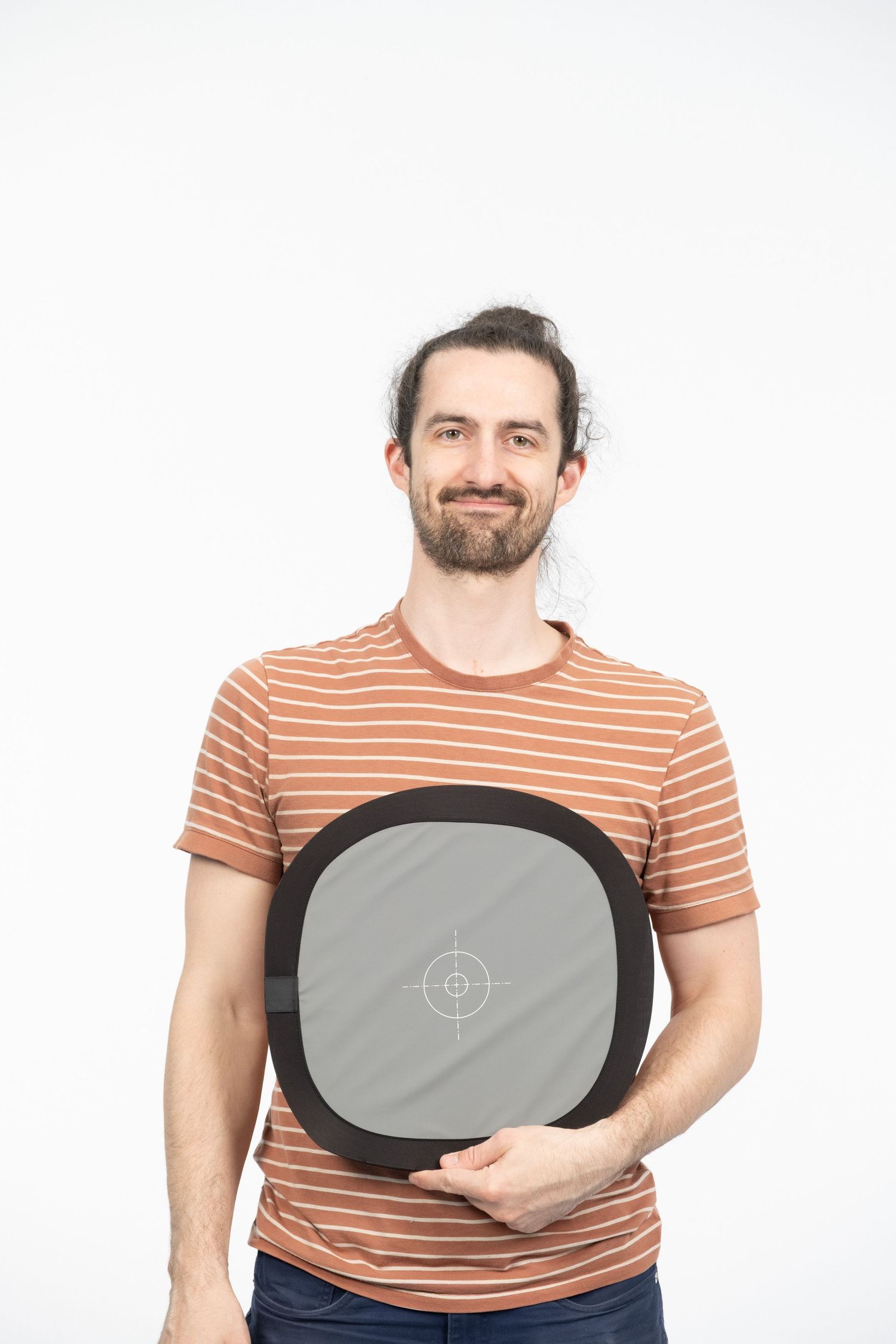 Luke, the photographer, in orange striped shirt demonstrates holding grey card against white background.