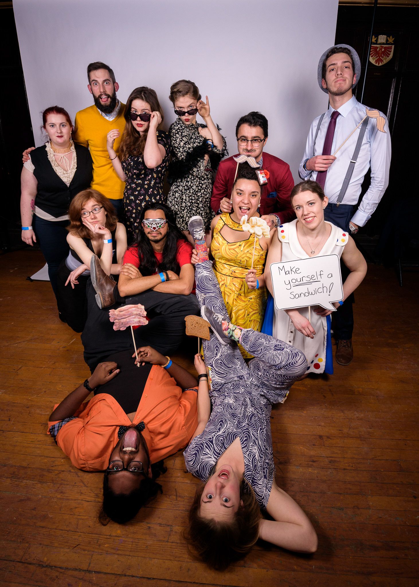 Group photo of party guests in vintage-inspired outfits sitting on wooden floor at dance event.