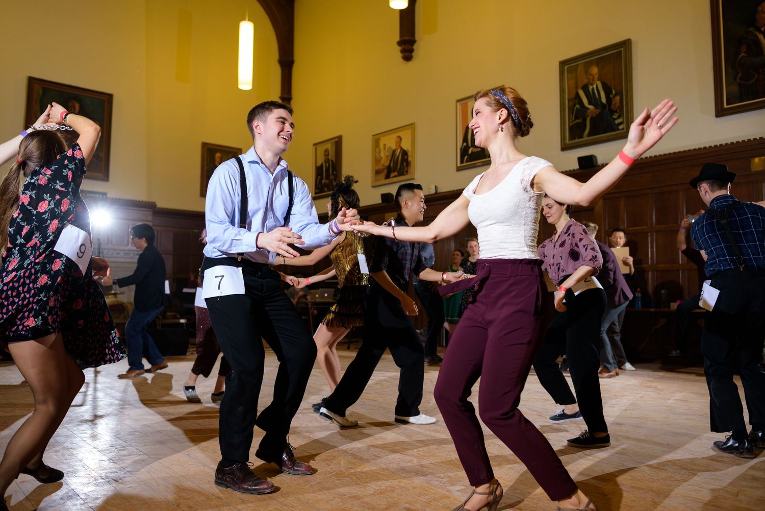 Dancers practising swing dance moves in a bright studio with wooden floors and pendant lighting.