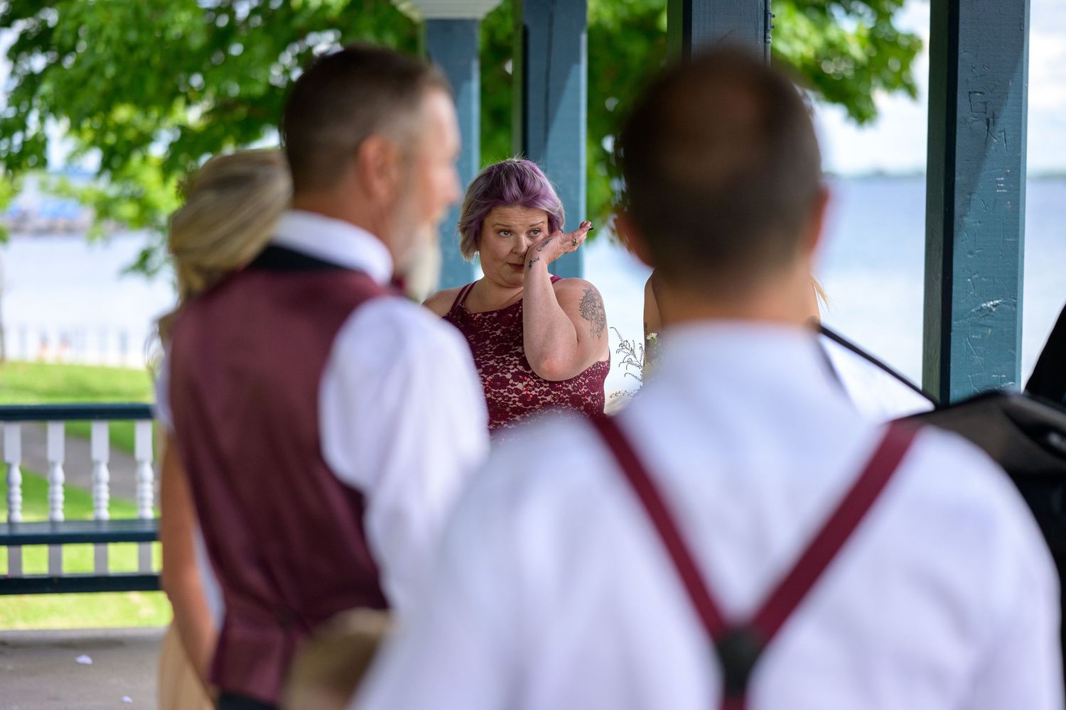 Emotional moment captured during outdoor wedding ceremony with attendees in burgundy attire.