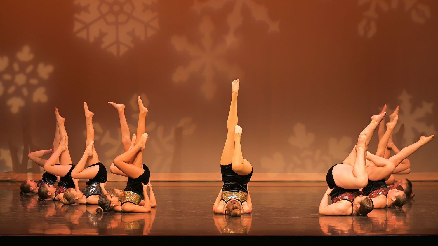 Dancers perform a synchronized routine on stage with dramatic lighting.