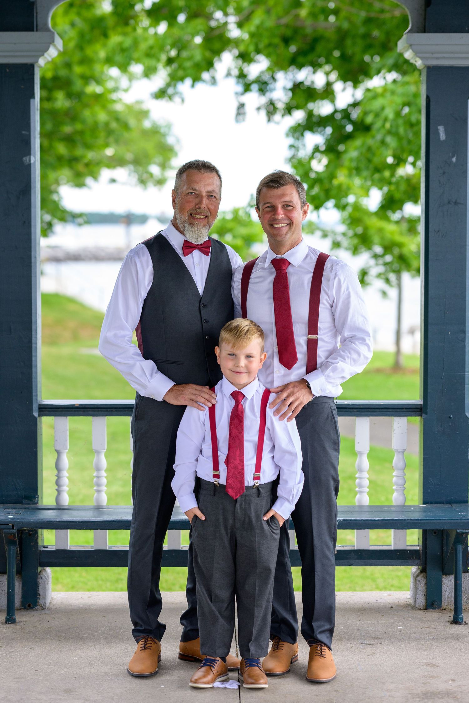 Three generations pose together in coordinating formal wear with red accessories on a gazebo.
