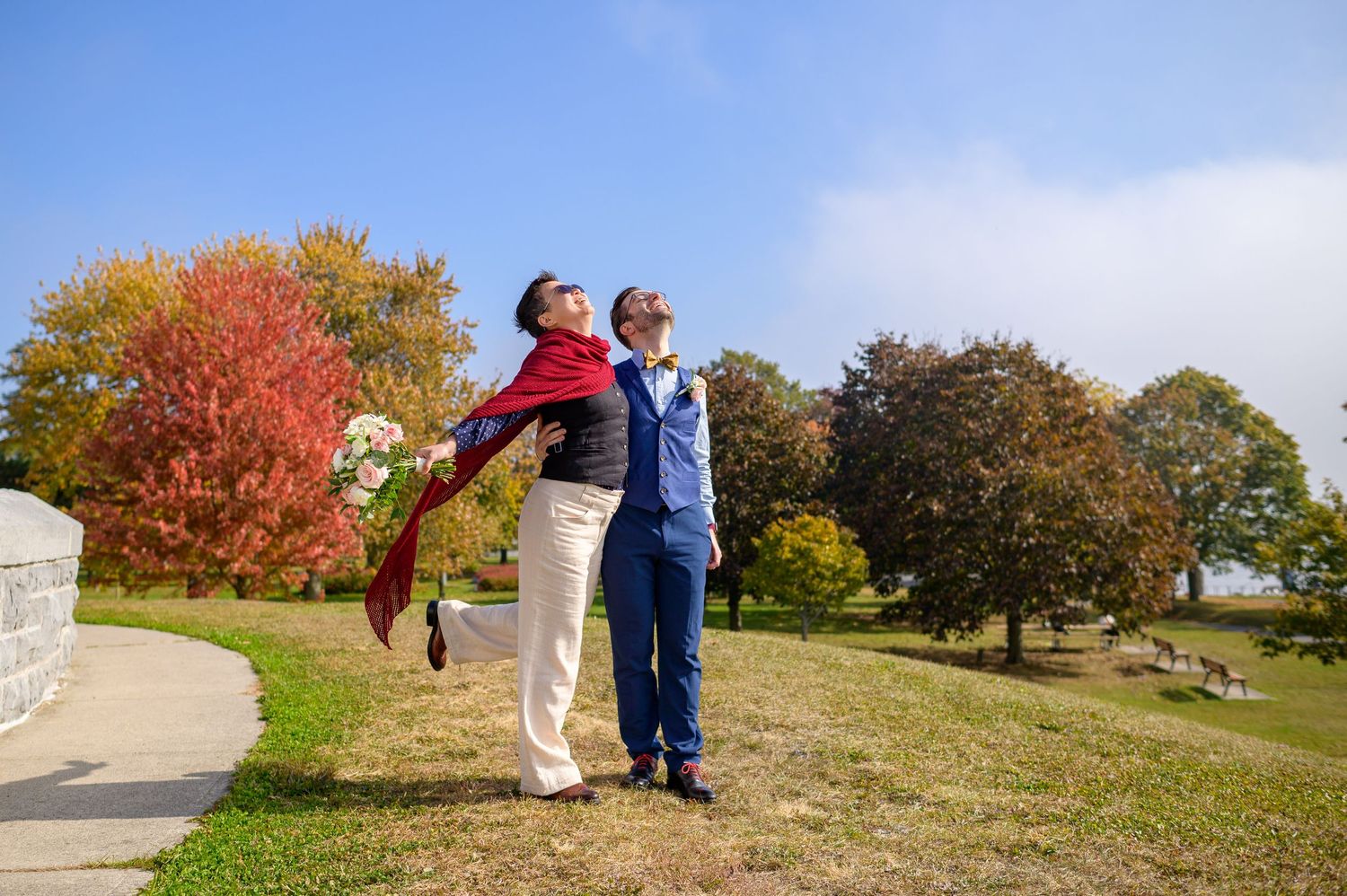 A couple shares a joyful moment outdoors during autumn with colourful fall foliage in the background.