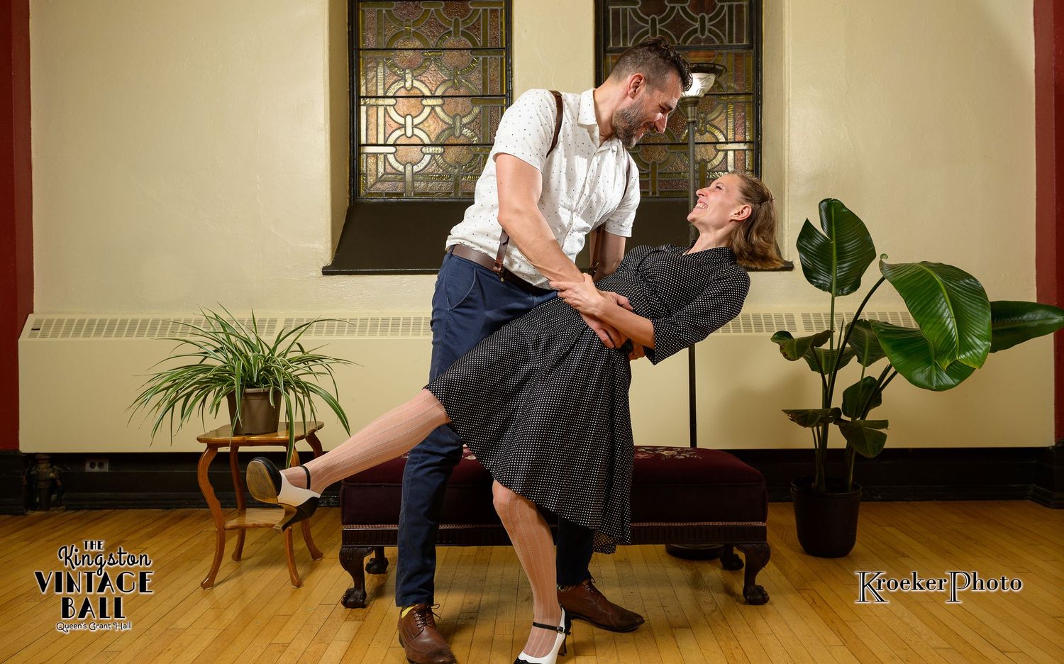 A couple performs a dramatic dance dip move in an elegant indoor setting with potted plants.
