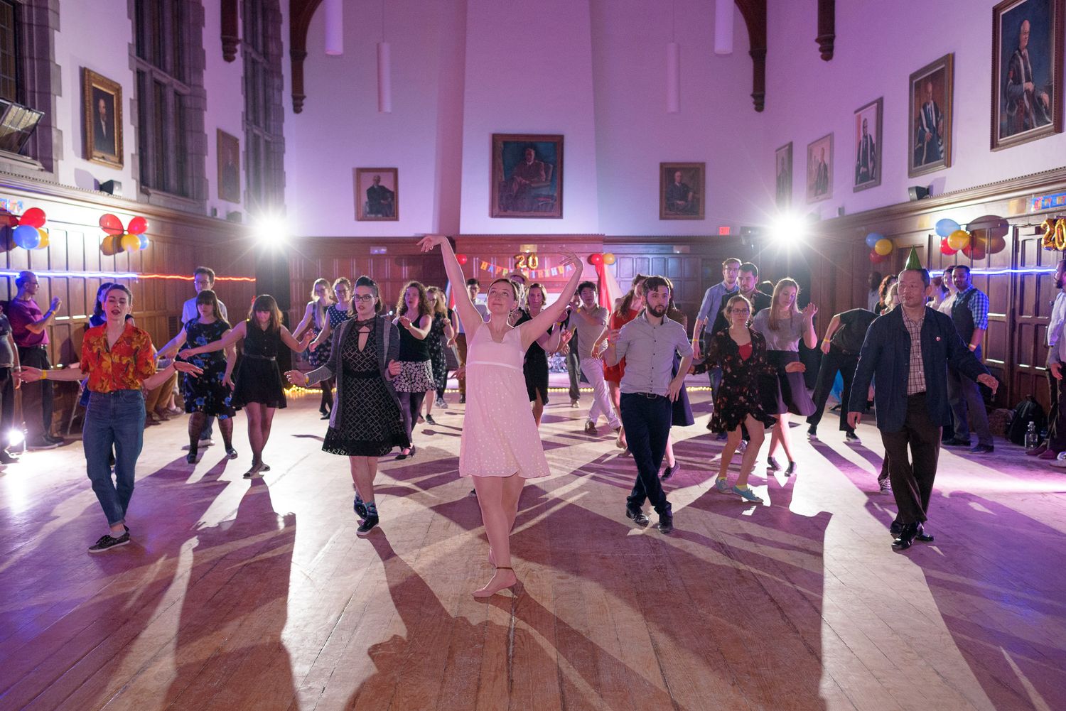 Dance event in a purple-lit ballroom showing multiple couples moving across the dance floor.
