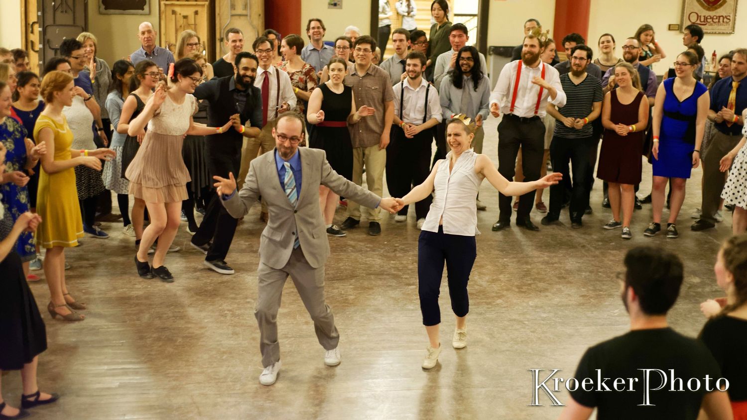 Dancers in vintage attire perform swing dance moves in a large ballroom setting.