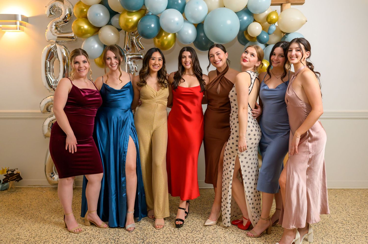 Group photo showing people in colourful formal dresses lined up against a light coloured wall.