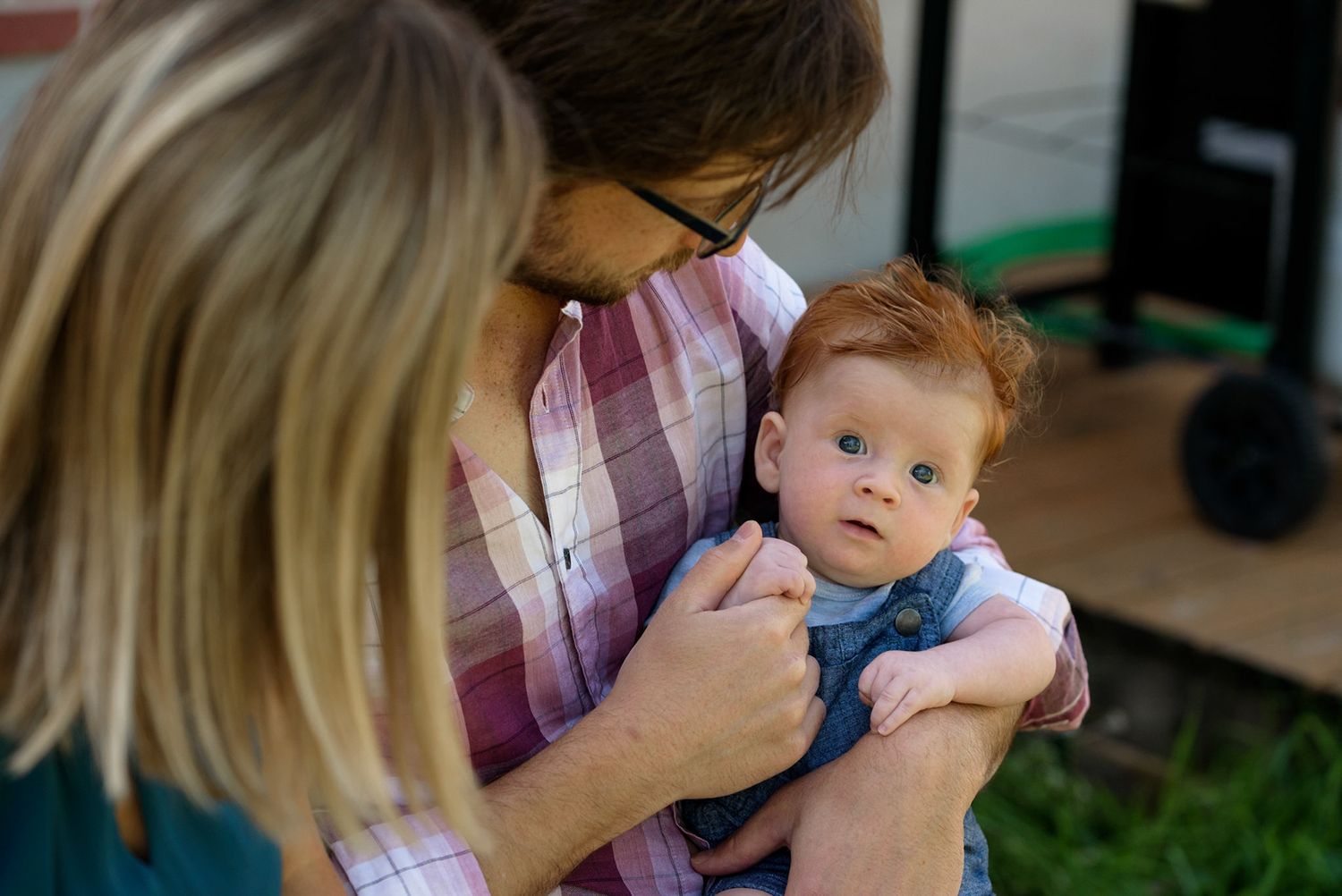 Father holds his baby, looking at the camera, while his wife looks at the baby.