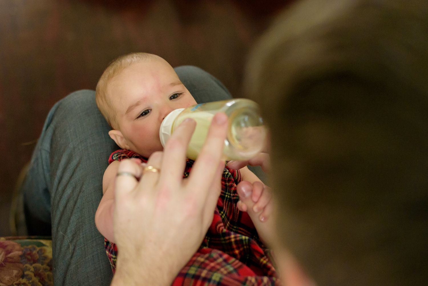 A baby drinks from a bottle while being held in her father's arms.