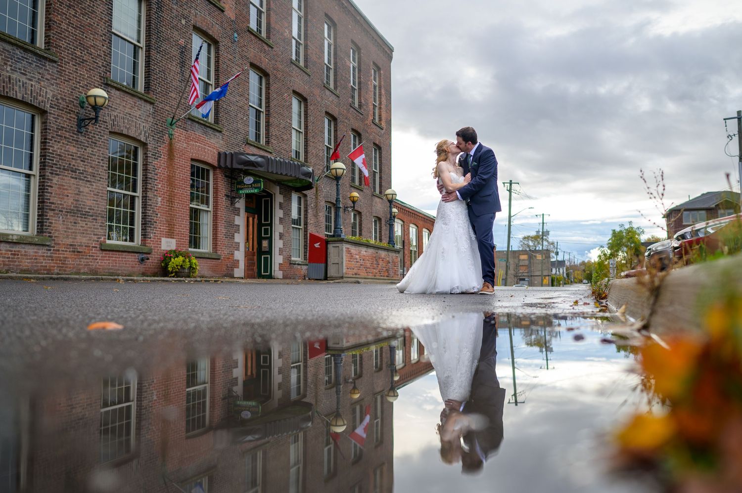 Romantic wedding photo with reflection in puddle outside historic building with flags.