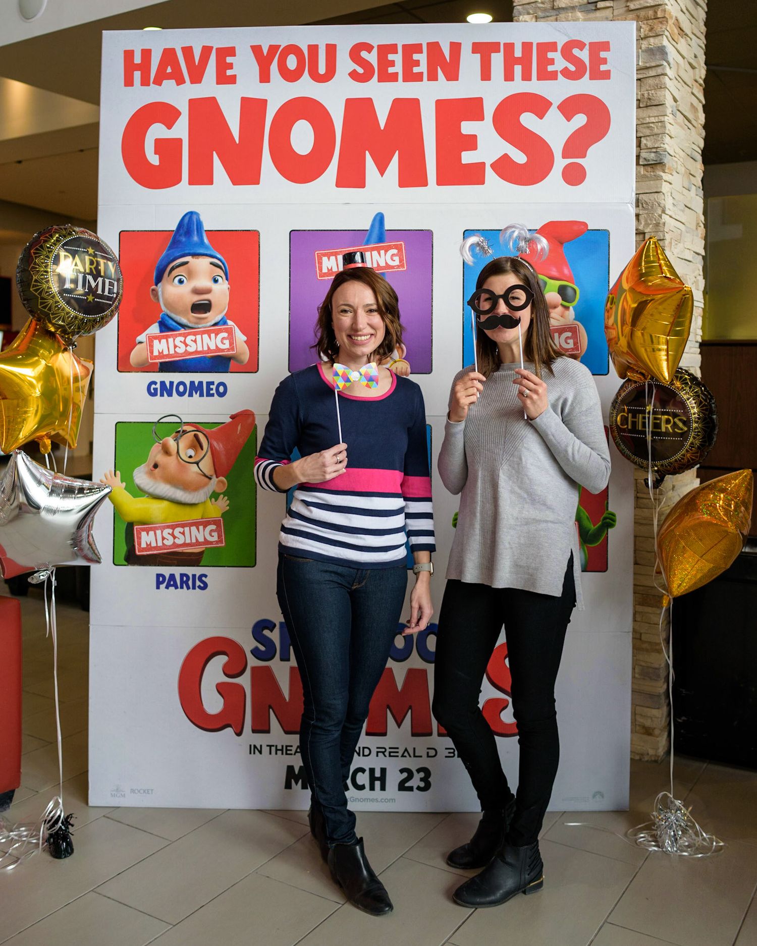Two people pose playfully in front of a 'Have You Seen These Gnomes?' movie poster display.