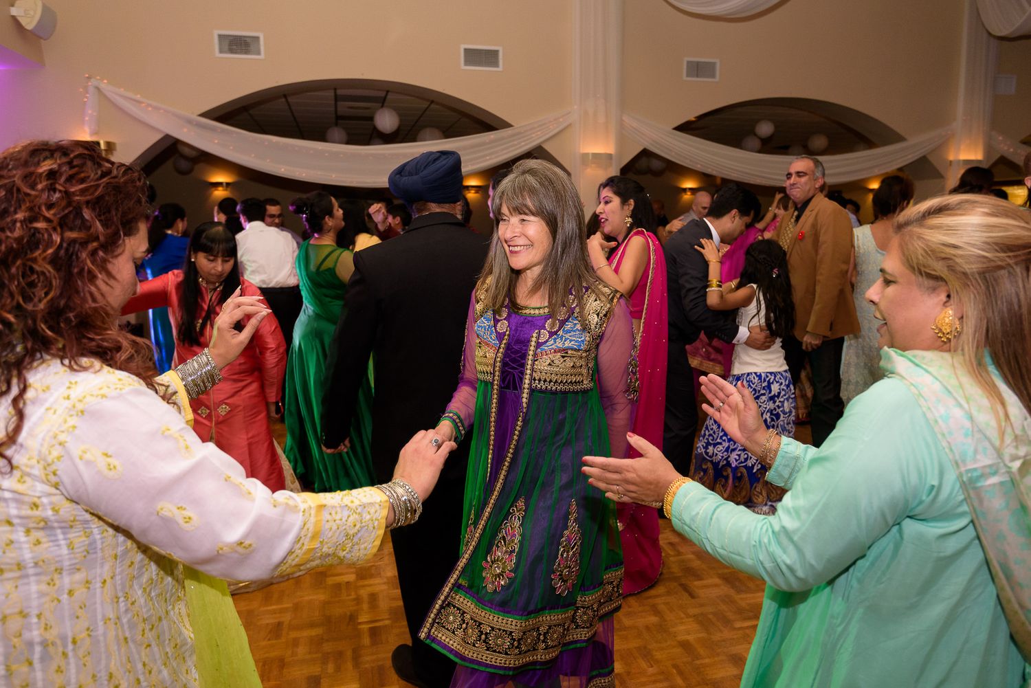 Wedding reception guests dance and celebrate in colourful traditional attire.